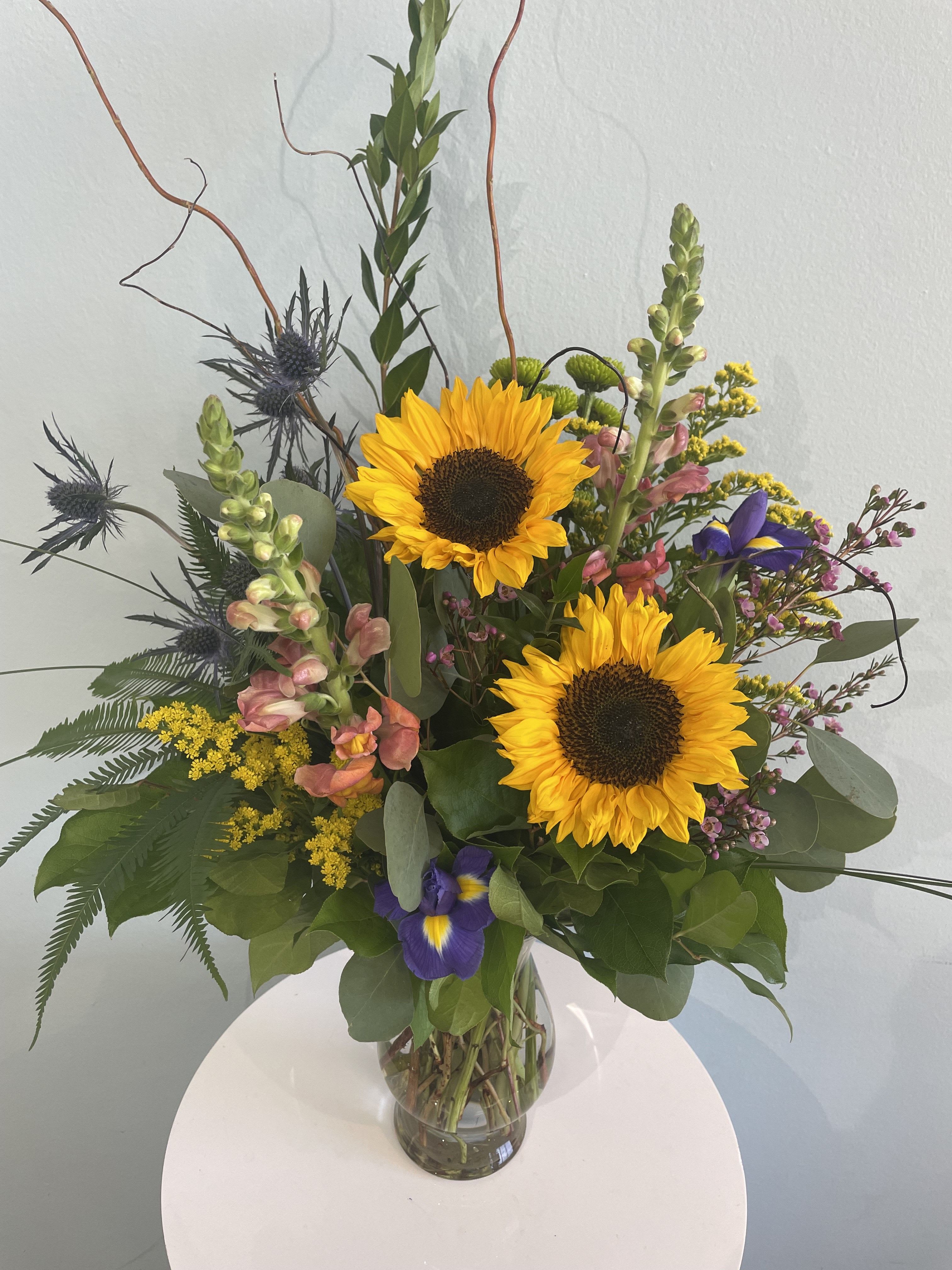 Sunflower Fields Sunflower Fields - This stunning wild-style arrangement features two bright sunflowers, and may include a mix of other flowers such as iris, snap dragons, and blue thistle. This arrangement is perfect for the Summer and Fall months. Brighten up anyone's day with this arrangement today!