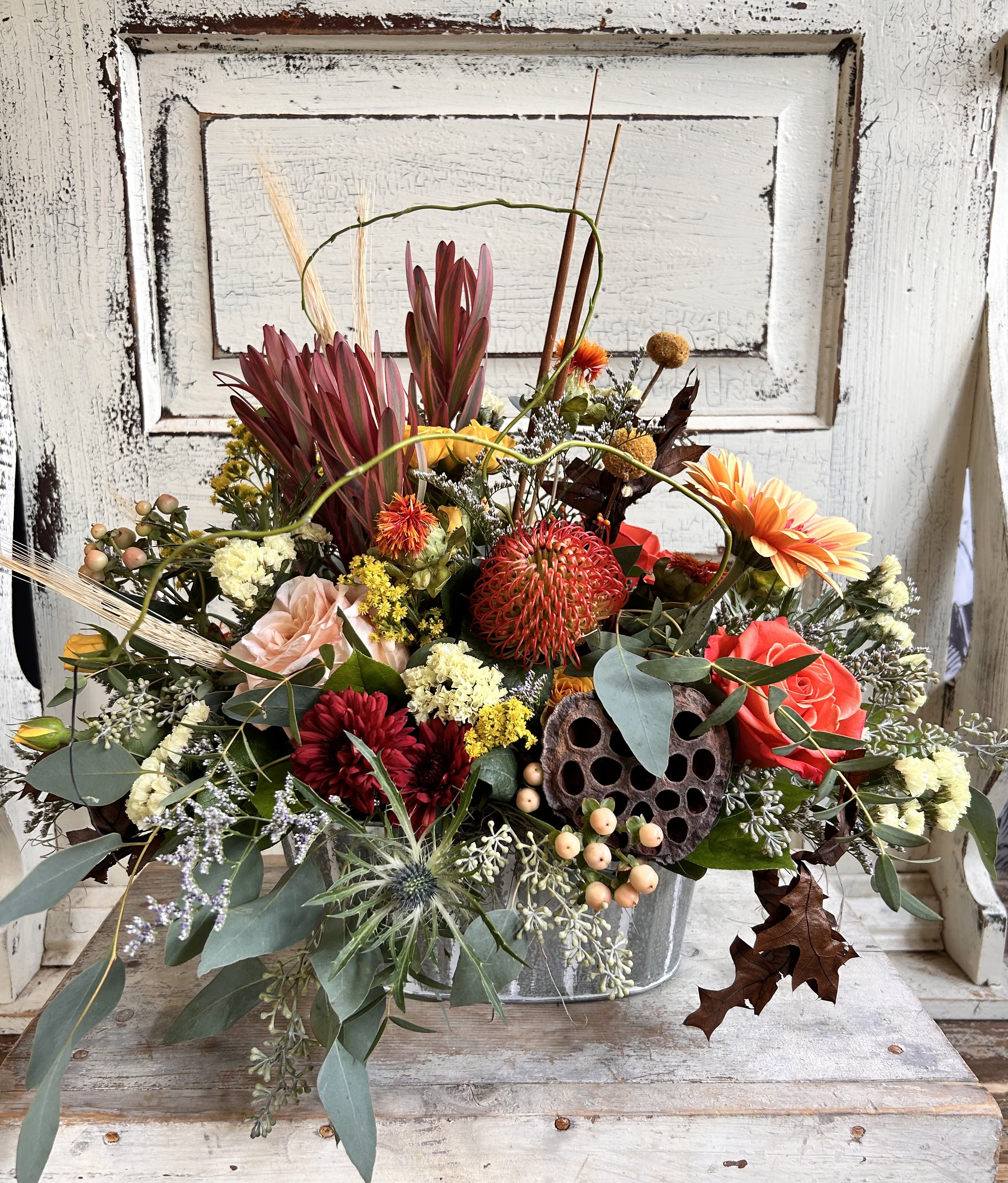 Textural Centerpiece - A metal or wooden container is designed with a unique assortment of seasonal blooms and foliage for a low and texture filled arrangement. Flower varieties and colors may vary slightly based on inventory.