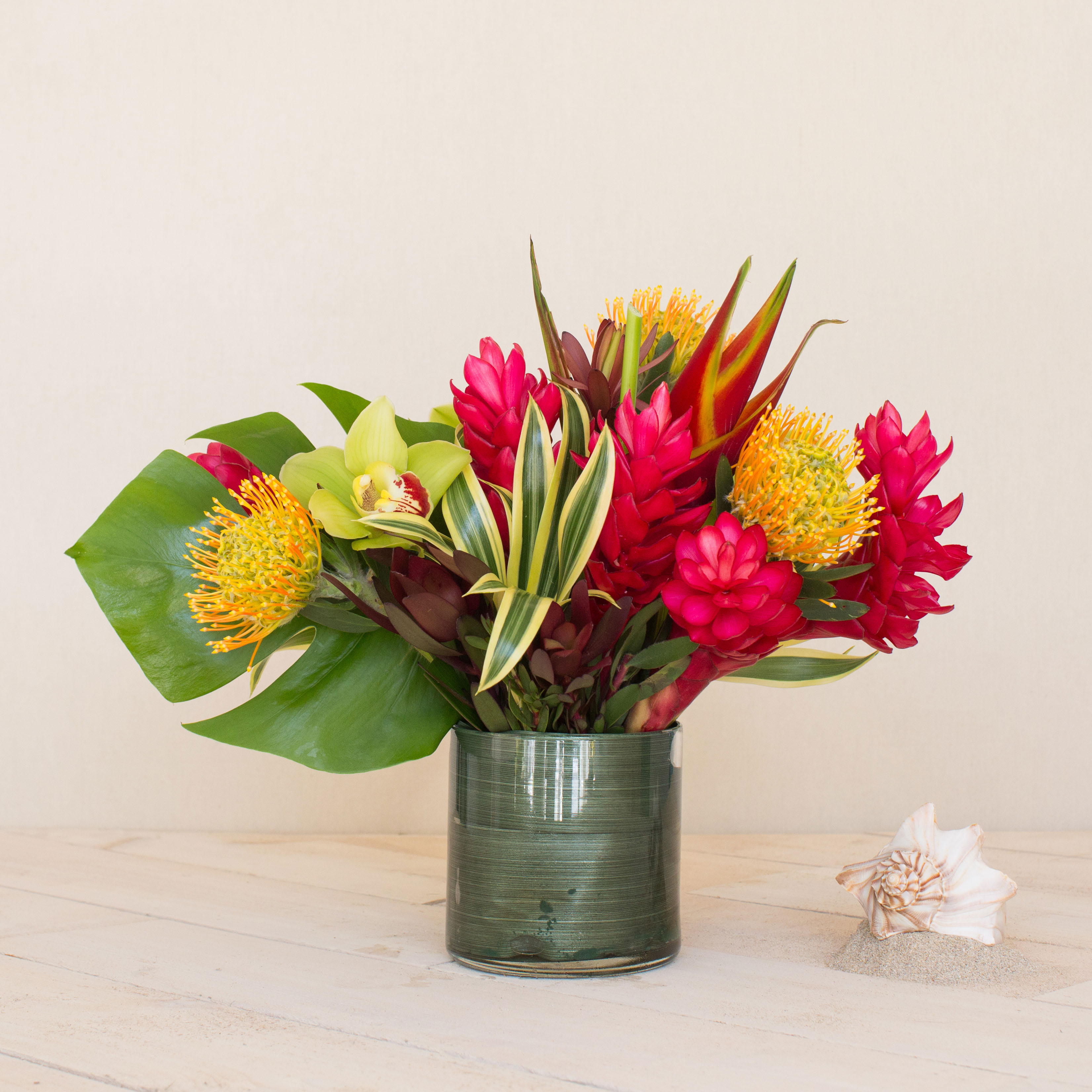 Tropical Bliss - Embrace the spirit of aloha with our contemporary arrangement that boasts a Hawaiian flair. This perfect gift features an assortment of locally grown tropical flowers, including ginger, protea, and elegant cymbidium orchids, creating a stunning and memorable display.  Key Features:  Locally Grown Tropical Flowers: Includes a variety of vibrant and exotic tropical flowers such as ginger and protea, sourced locally for freshness and authenticity.  Elegant Cymbidium Orchid: Accented with elegant cymbidium orchids, adding sophistication and grace to the arrangement.  Contemporary Design: Crafted in a modern style, combining Hawaiian influences with contemporary aesthetics for a unique and stylish gift.  Perfect Gift of Aloha: Ideal for expressing warmth, hospitality, and affection, making it a thoughtful gift for any occasion.  Versatile Presentation: Presented in a stylish container or vase, enhancing the beauty of the tropical blooms and ensuring an elegant presentation.  Celebrate the essence of aloha with our Contemporary Hawaiian Flair Arrangement, a beautiful expression of Hawaiian culture and natural beauty, perfect for gifting to convey heartfelt sentiments and warm wishes.