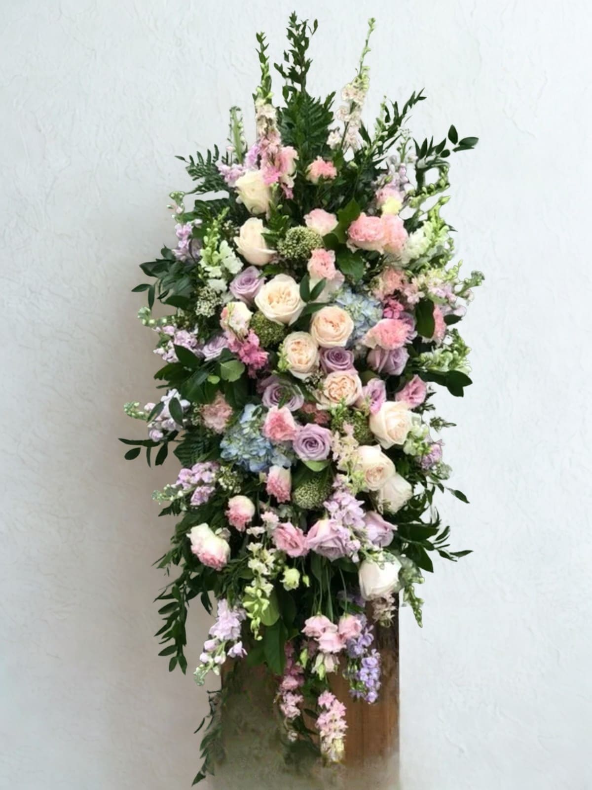Pastel Traditions Spray - A pastel color palette creates comfort and grace with this Traditions Spray. Featuring a selection of muted blossoms such as blush pink, lavender and ivory with spring greens. A beautiful way to remember a loved one.    Other color combinations available.  Please contact us for consultation and availability.