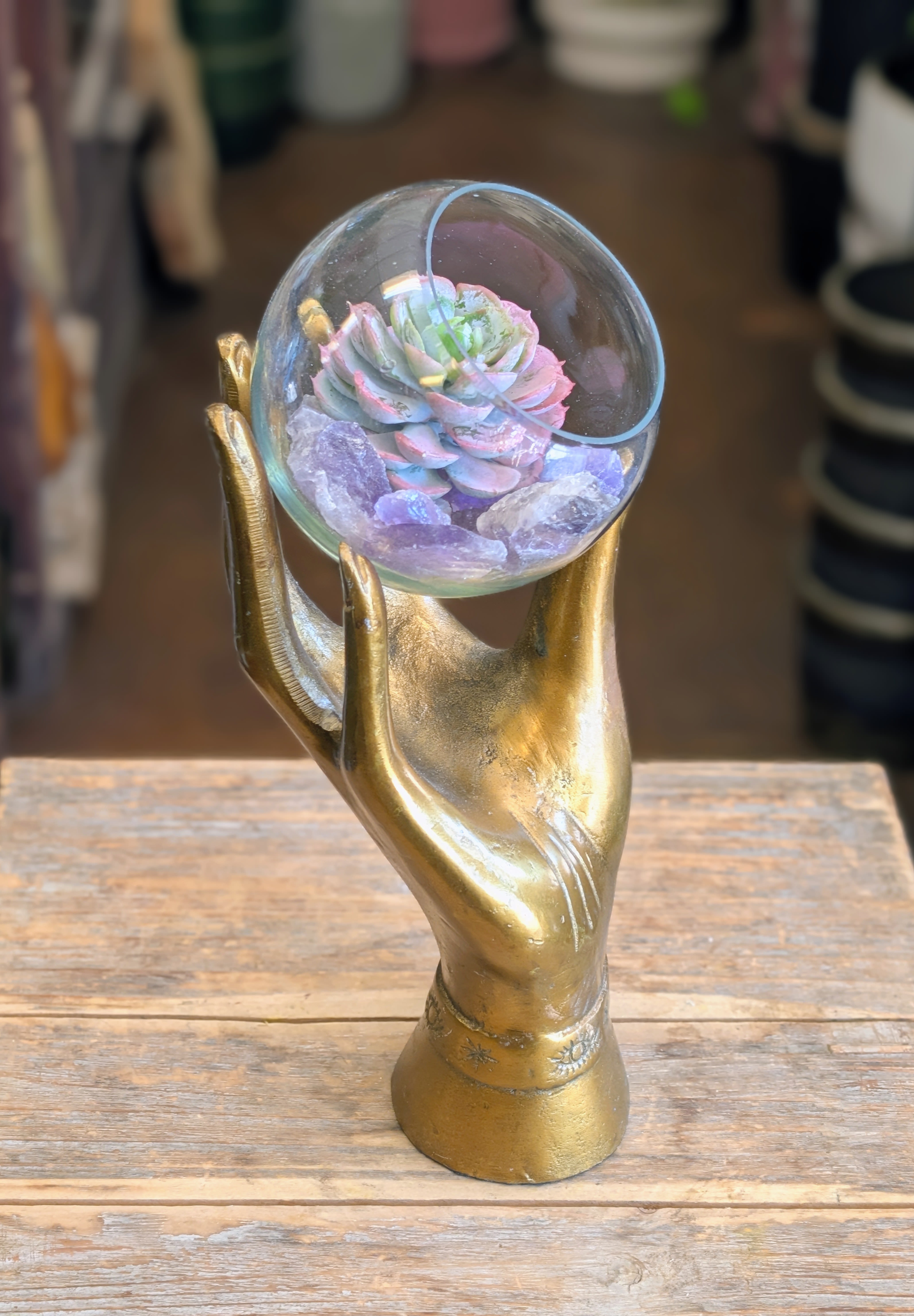 The Oracle- Faux Succulent and Raw Amethyst - The Oracle  A stunning fusion of art, energy, and nature — The Oracle is one of Windmill Floral Expressions’ most captivating creations. This sculptural piece features a golden metal hand gracefully holding a glass orb filled with a faux succulent and raw amethyst crystals. Symbolizing intuition, healing, and protection, it brings a touch of mysticism and serenity to any space.  Perfect as a gift for crystal lovers, spiritual seekers, or modern bohemians, this one-of-a-kind design blends botanical beauty with mystical energy. Ideal for desks, meditation corners, or sacred spaces, The Oracle reflects the artistry and intention behind every creation at Windmill Floral Expressions.  Custom designed in Henderson, Nevada Available for local delivery or pickup Explore our collection of mystical gifts, permanent botanicals, and inspired décor — exclusively at Windmill Floral Expressions.  Please note this is an artificial succulent.