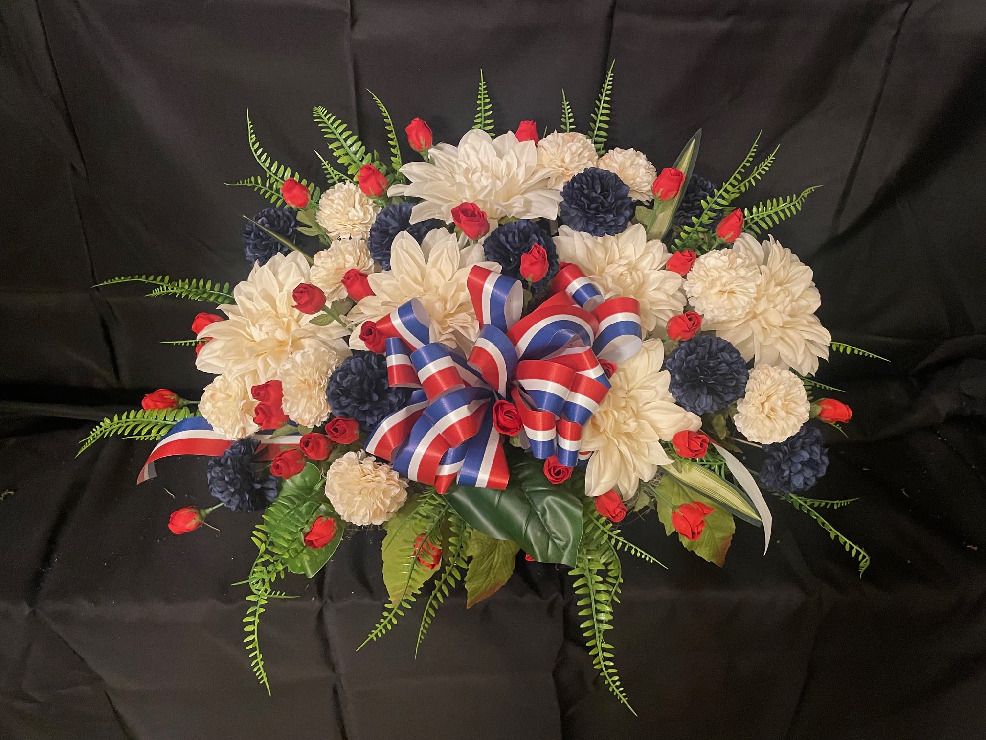 Gravestone Saddle, Patriotic - This arrangement is made to sit atop your loved one's gravestone. Handmade inhouse of artificial flowers. It's on an adjustable base to make for an easy fit. This Item is for pick-up only. If you'd like it delivered to a cemetery, please call 814.536.0536