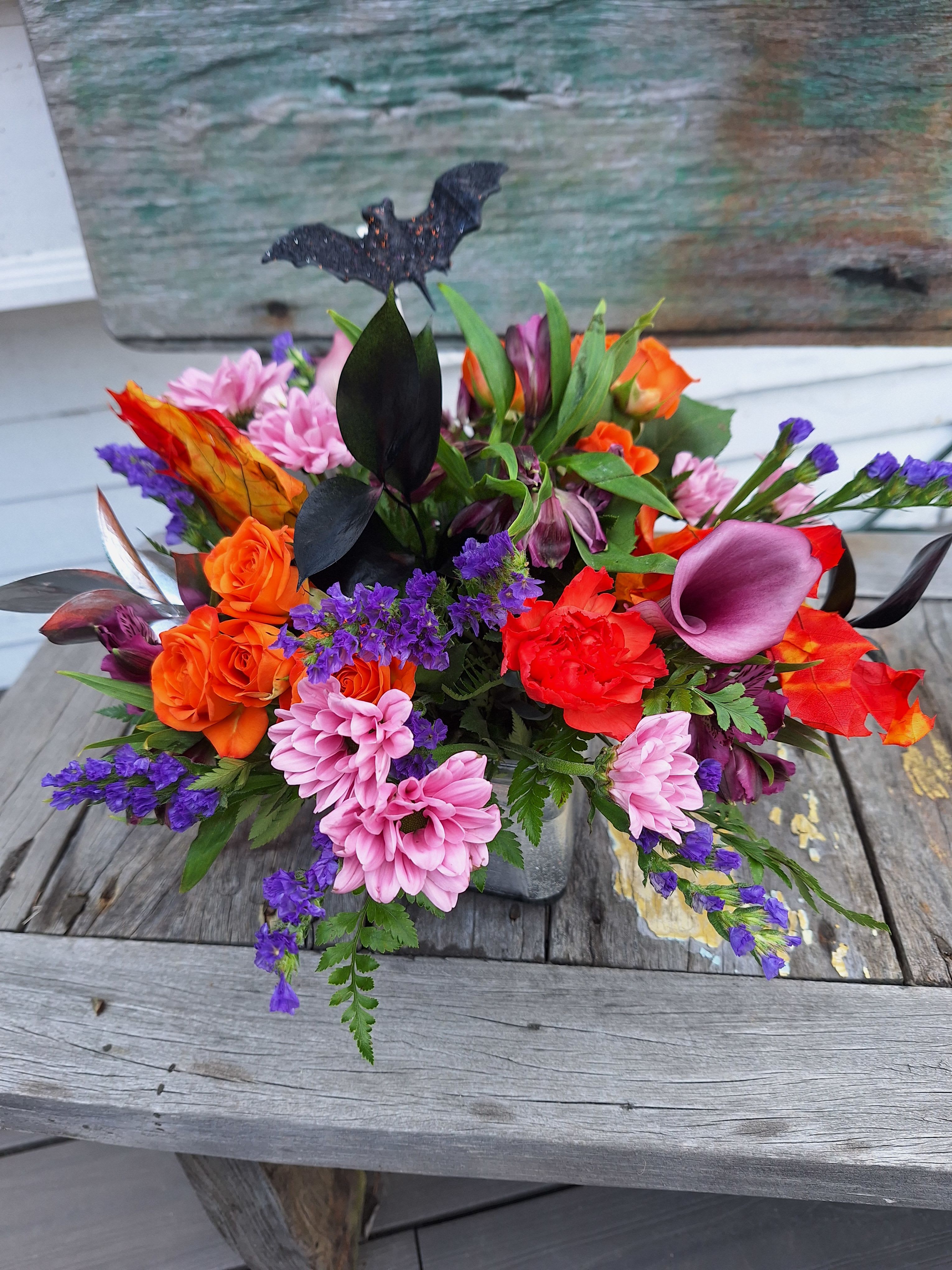 Hocus Pocus Bouquet Hocus Pocus Bouquet - Lavender calla lilies, orange spray roses, lavender daisys, lavender alstro, orange carnations, purple status, faux leaves and a spooky spider arranged in a glass cube lined with silver ty leaf