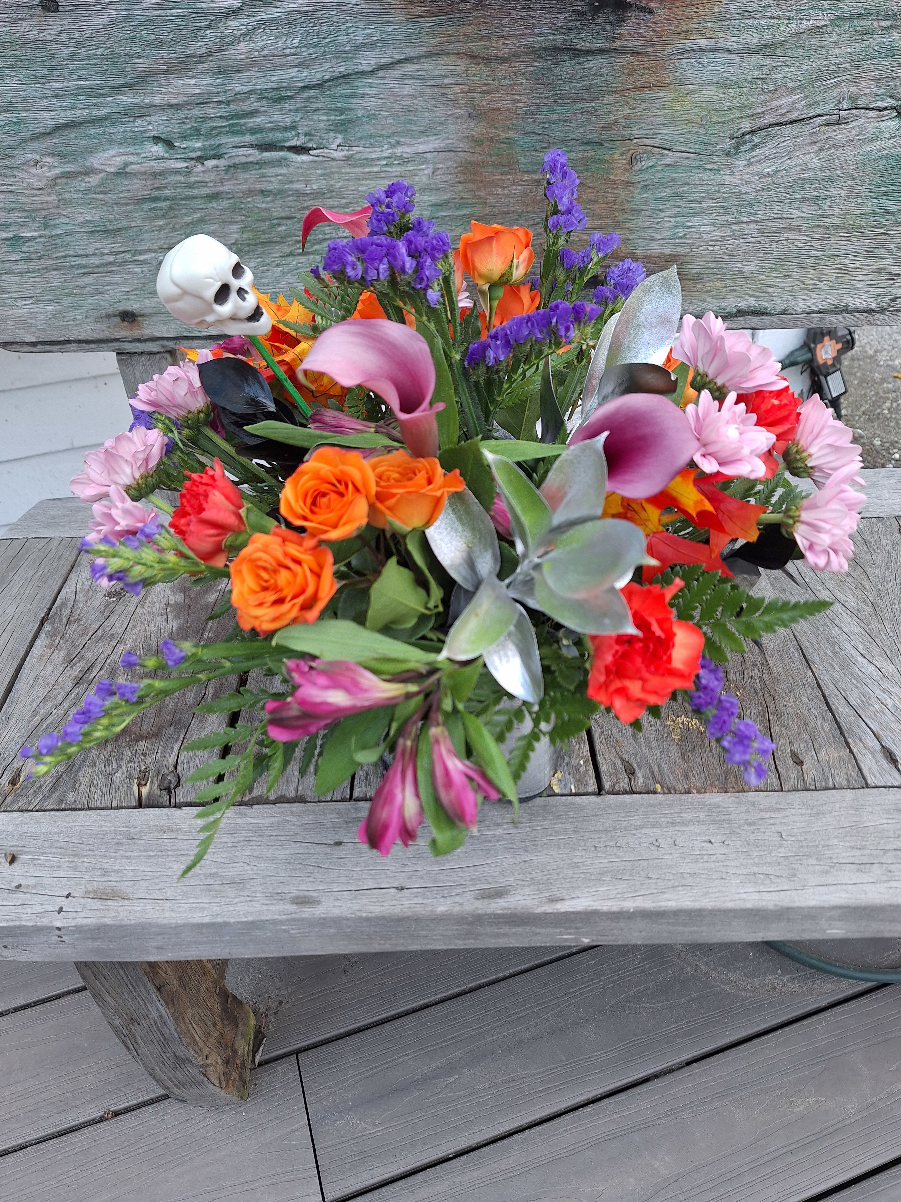 Hocus Pocus Bouquet-2 - Lavender calla lilies, orange spray roses, lavender daisys, lavender alstro, orange carnations, purple status, faux leaves and a skeleton head arranged in a glass cube lined with silver ty leaf