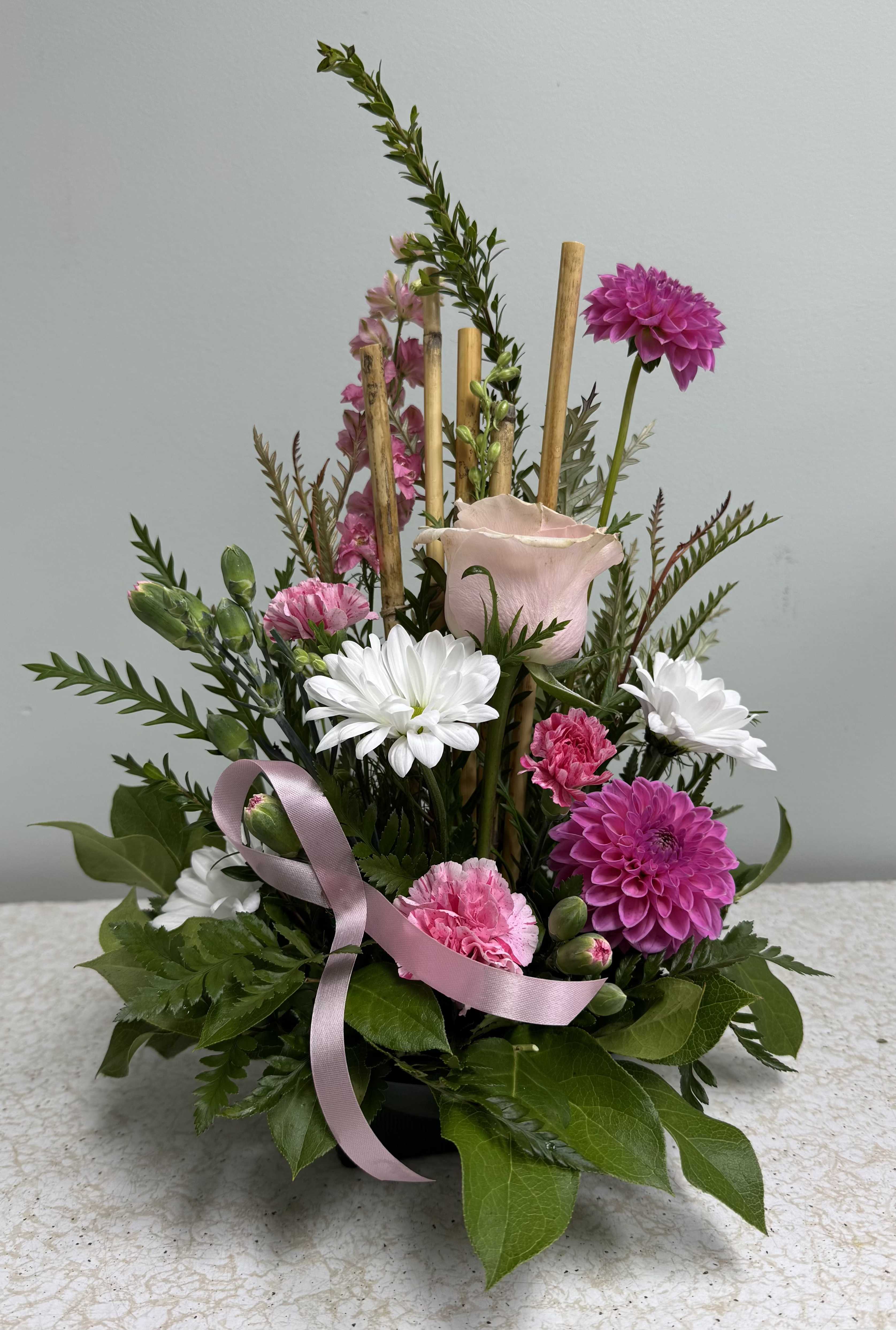 Breast Cancer Awareness Arrangement Breast Cancer Awareness Arrangement - This small piece is a touching tribute to those who have been affected by breast cancer. It features one pink rose, pink dahlias (while the frost holds off), pink larkspur or snapdragon, pink carnations, and white daisies. Comes with a pink ribbon and bamboo accents.