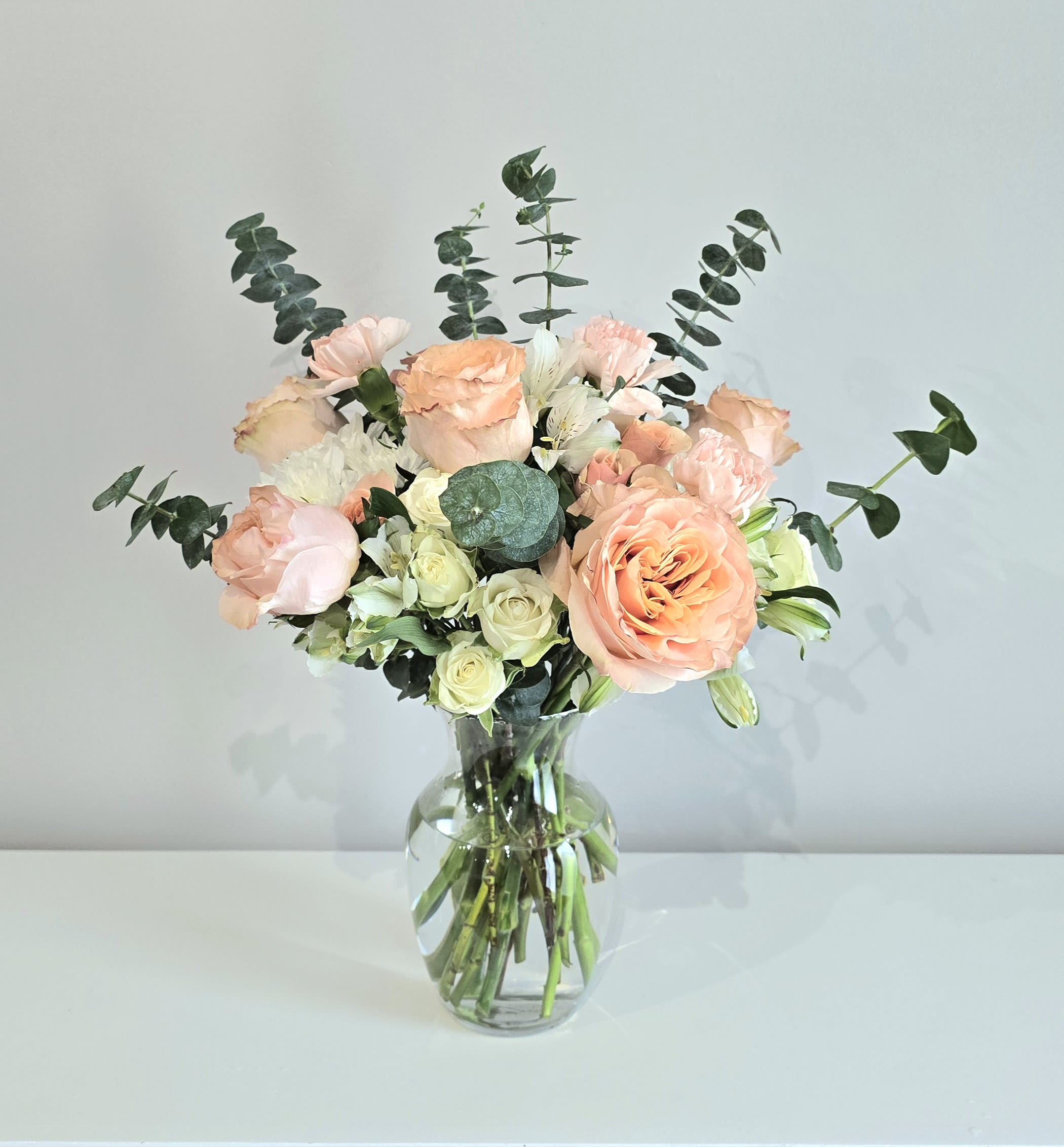 Peaches & Cream Peaches & Cream - A beautiful bouquet full of peach & white blooms including roses, carnations, alstroemeria. Accented with fragrant spiral eucalyptus. Delivered in a classy clear glass couture vase. A classic choice that's perfect for all occasions. Measures approx. 19" tall and 15" wide Orientation: All around