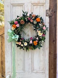 Norwegian Wood - A humble floral wreath made using seasonal flowers and greenery adorned with a bow. This can be made to hang on a door for a celebration or on a stand for a memorial. 