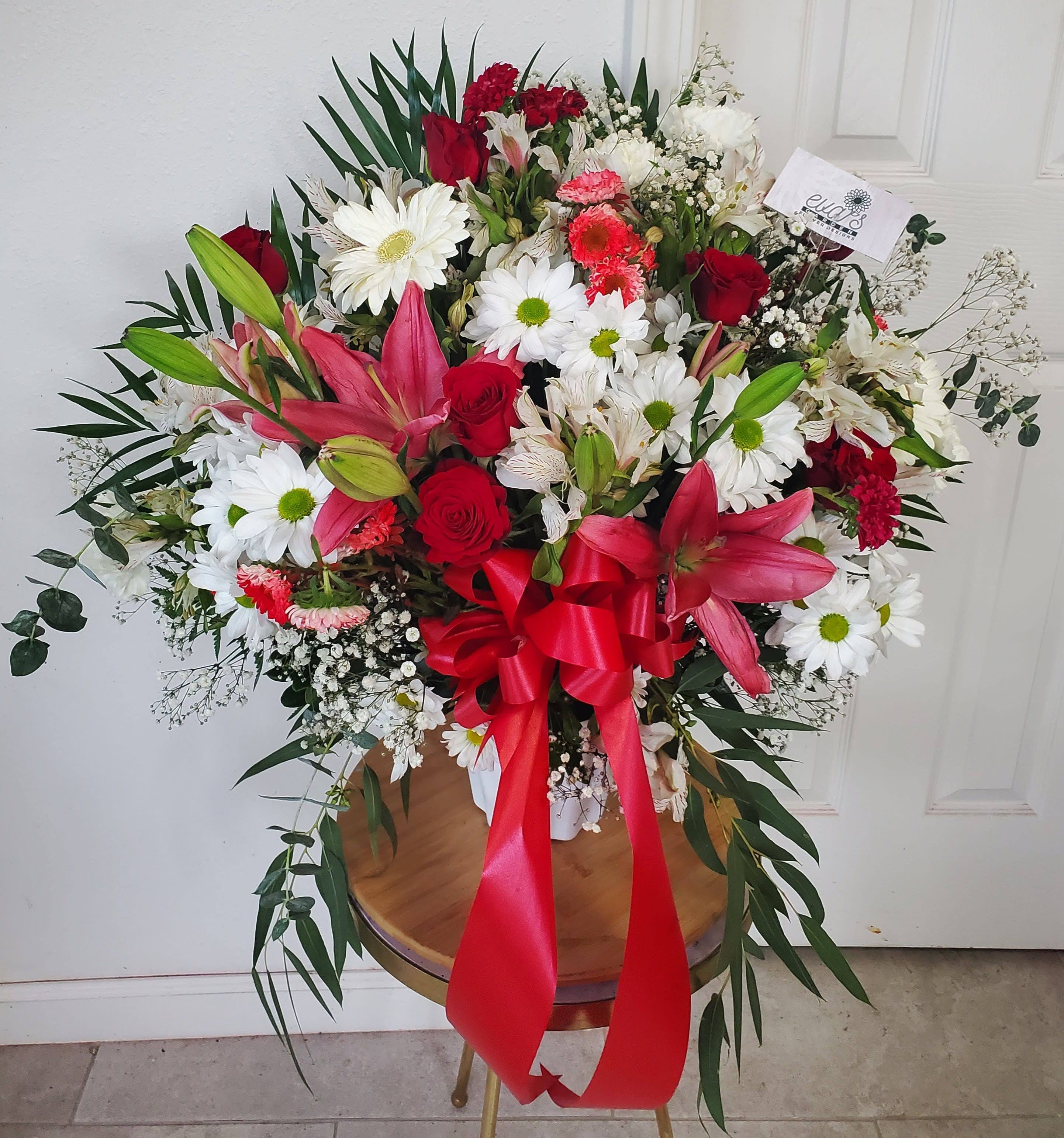 Pink, Red, &amp; White Standing Basket - White plastic vase filled with a radiant assortment of 6 red roses, 2 stems of pink asiatic lilies, white daisies, white alstroemeria, red aster matsumoto, gypsophila, pittosporum, eucalyptus, and cambray palm.  (Picture depicts a standard product; deluxe &amp; premium size available upon request)