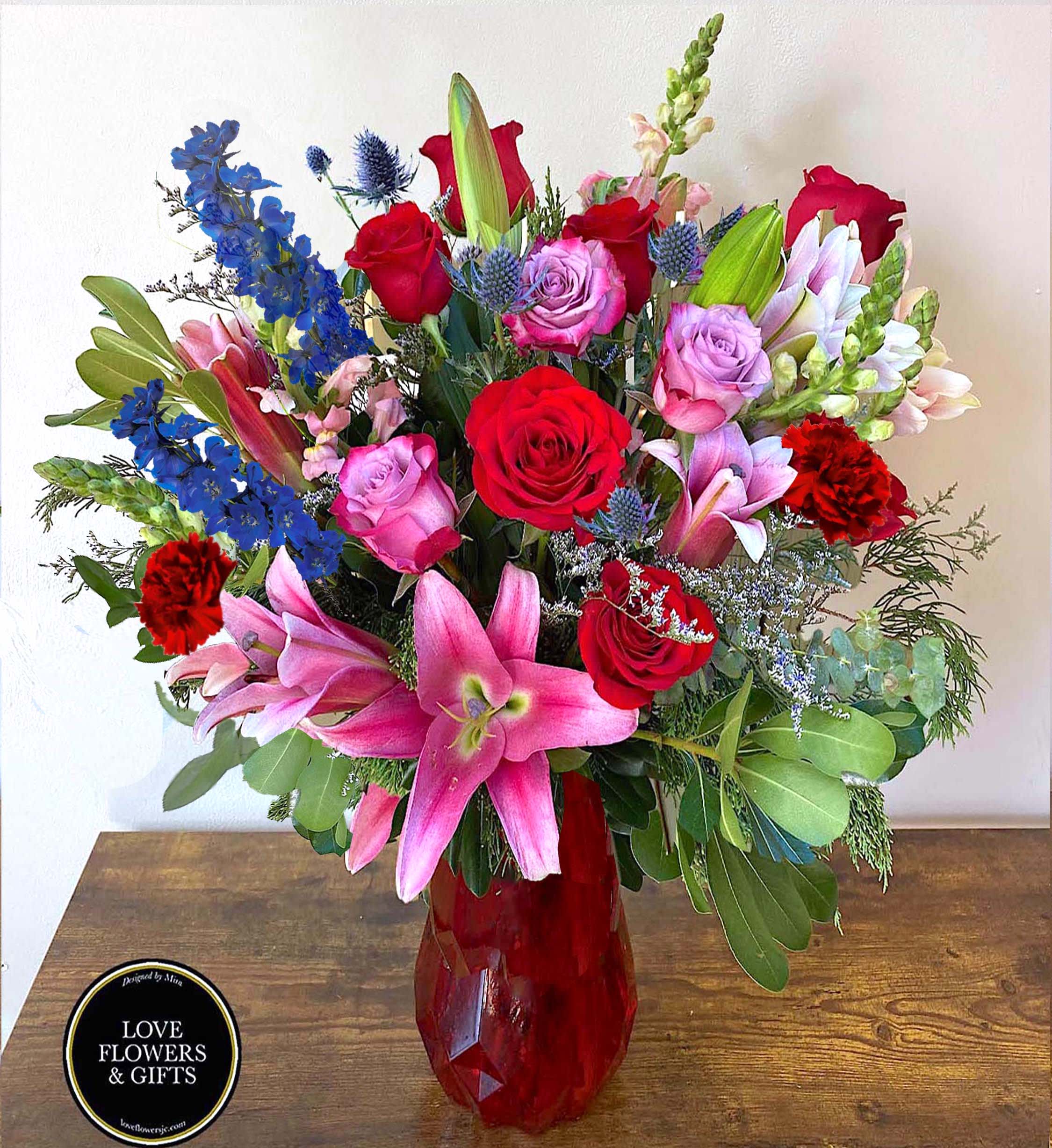 Divine Love Divine Love - A large romantic arrangement, full of love. Designed in a high-quality red glass vase. Made of pink lilies, red and purple/pink roses, snapdragons, limonium, and pops of blue flowers with greenery.