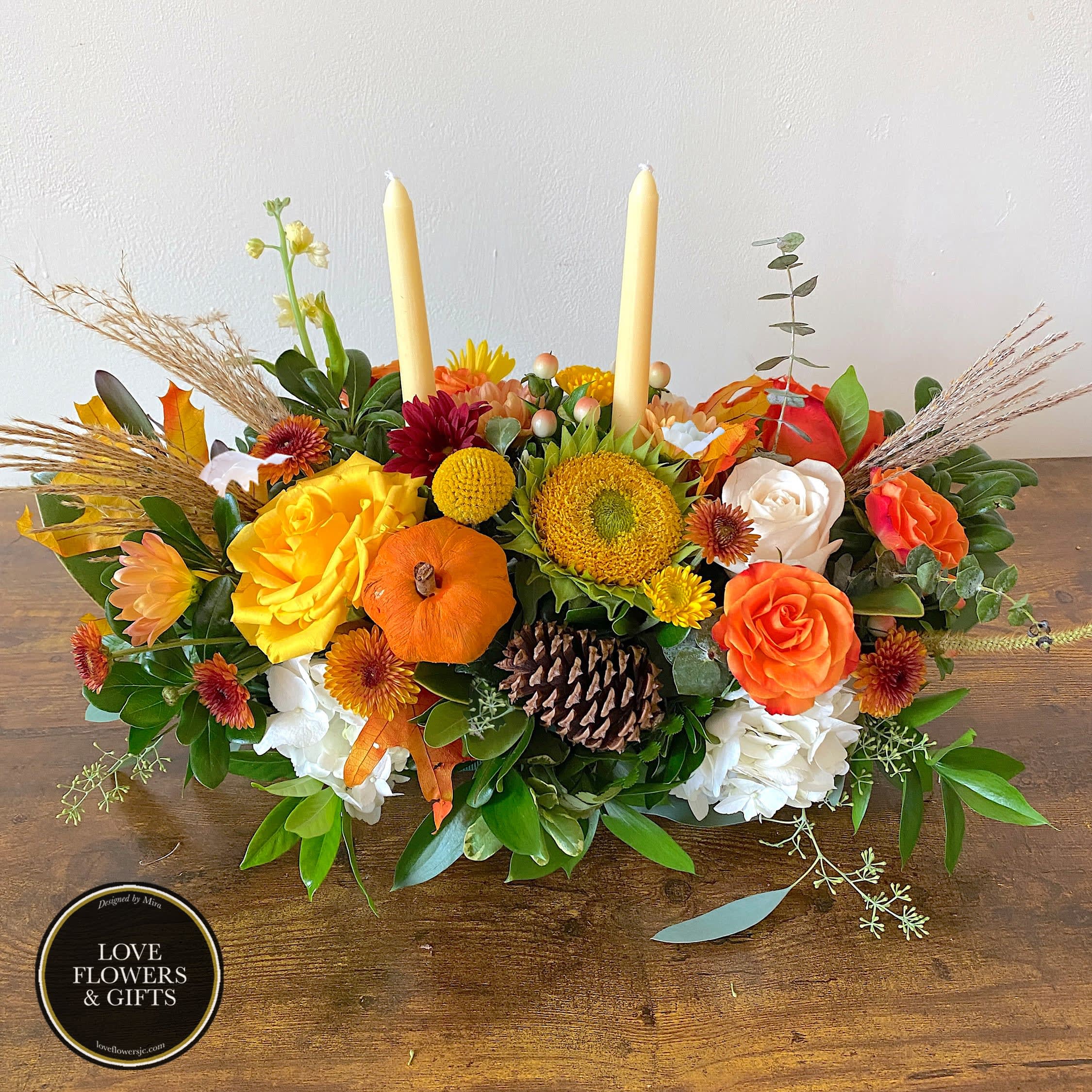 Sweet Pumpkin Centerpiece  - A modern autumn low centerpiece, with softer and brighter autumn colors of yellow, orange, and whites in a bed of fresh greenery with preserved elements for more seasonal vibes, designed with cream tall wax candles.   Perfect for small and big seasonals parties and gatherings or to cheer up the dinner table!