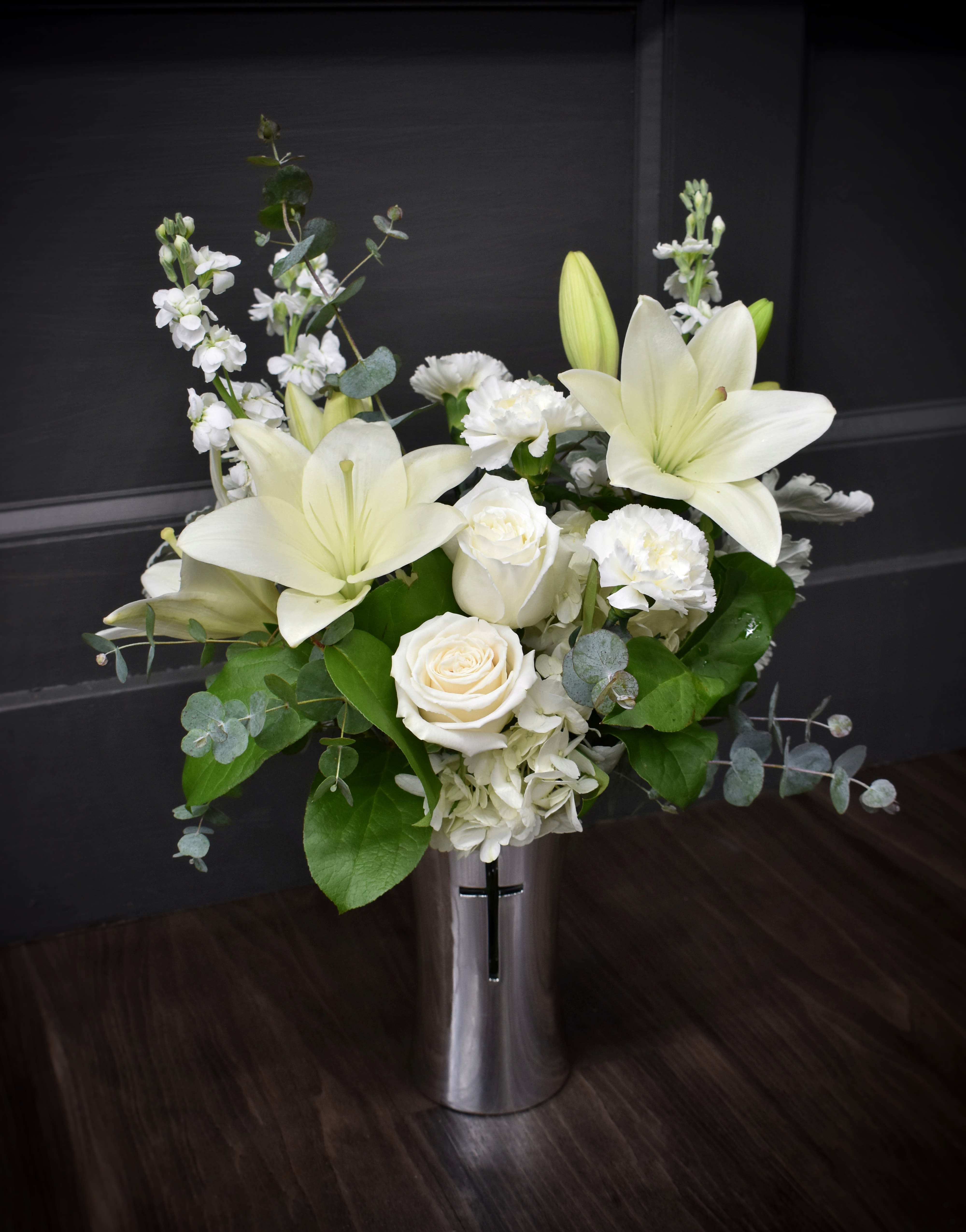 Reflections of hope  Reflections of hope  - An elegant tribute to a loved one in a silver container, featuring a cross. This reflective container is a reminder to reflect on the blessing of life.  This piece is arranged with hydrangea, roses, stock, lilies, and carnations, all in white.
