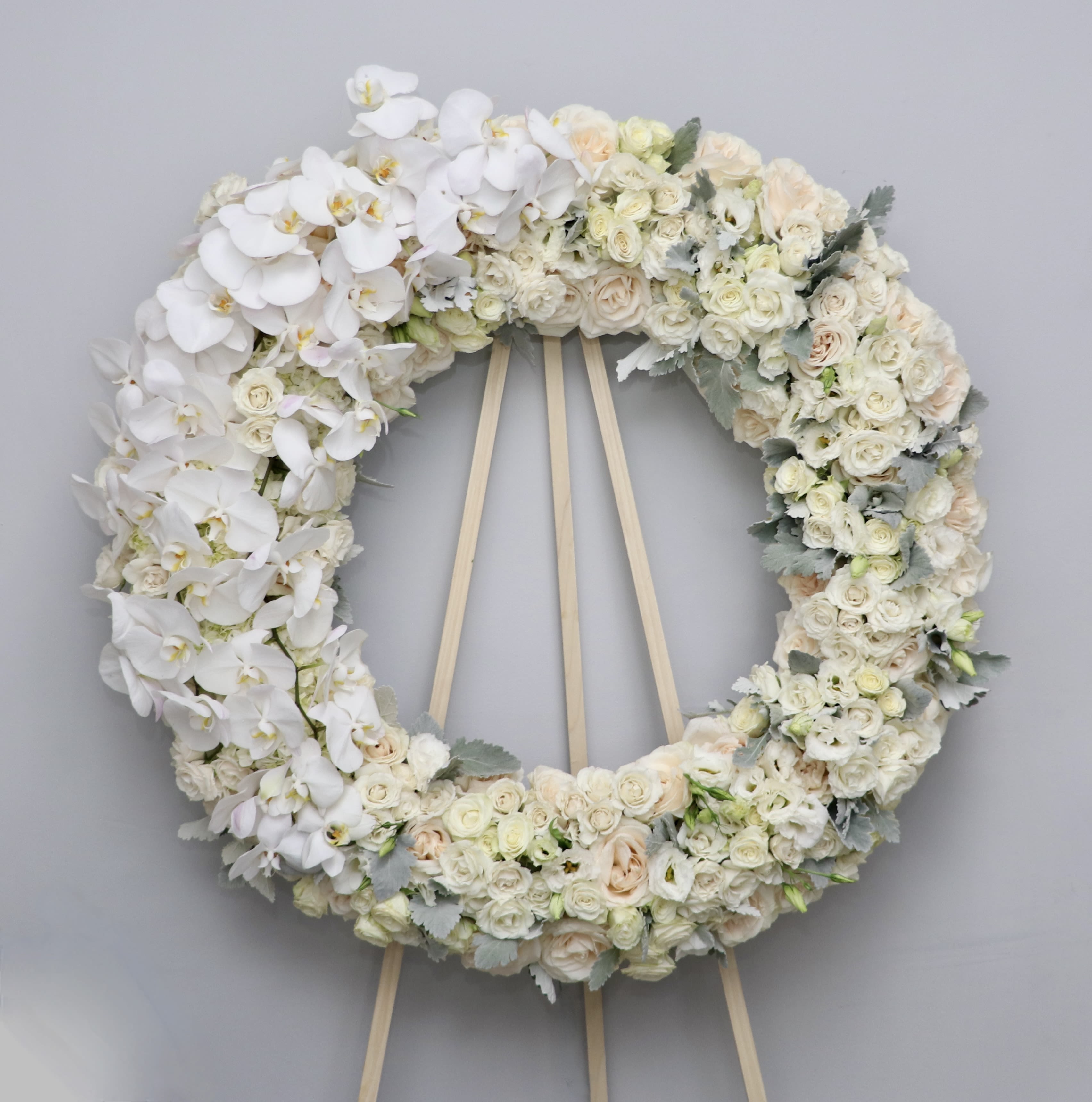 White Orchid Wreath - This white wreath is made with all white florals and features white orchids cascading down one side and cooler, frosted greenery.  We include easel, printed banner and delivery (some fees may apply). An additional banner can be added for $15.  Standard size is 30'', deluxe is 36'', and premium is 42&quot;