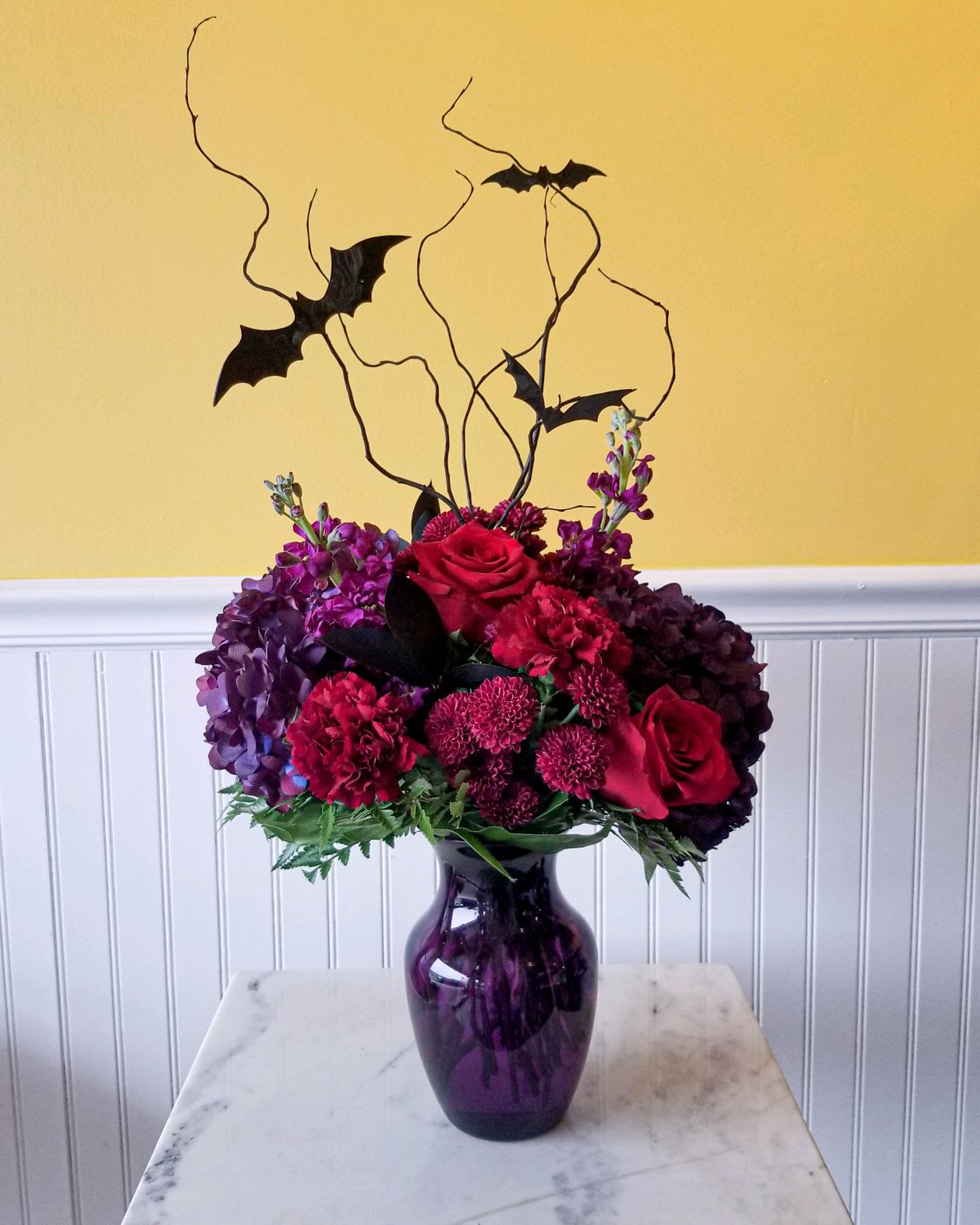 Hallows Eve Hallows Eve - Dark and mysterious blooms in a purple vase adorned with black bats. Perfect for the Halloween lovers out there!