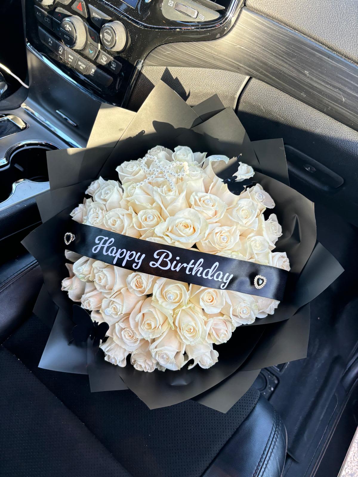 Elegant White 50 Rose Birthday Bouquet / Ramo de 50 Rosas Blancas de Cumpleaños - Elegant White Rose Birthday Bouquet / Ramo de Rosas Blancas de Cumpleaños  A stunning arrangement of soft white roses wrapped in sleek black paper, symbolizing elegance and sophistication. Accented with a “Happy Birthday” ribbon and delicate pearl details, this bouquet makes any celebration unforgettable — perfect for someone who loves timeless beauty.  Un impresionante ramo de rosas blancas envueltas en elegante papel negro, símbolo de pureza y sofisticación. Decorado con cinta “Happy Birthday” y delicados detalles de perlas, este arreglo es ideal para regalar en un cumpleaños especial lleno de estilo y elegancia.  Perfect for / Perfecto para: Birthdays, celebrations, or elegant surprises. Includes / Incluye: Fresh white roses, black waterproof wrap, decorative ribbon, and pearl accents. Note / Nota: Wrapping is waterproof; keeping it on is optional. Trim stems and change water every 1–2 days.