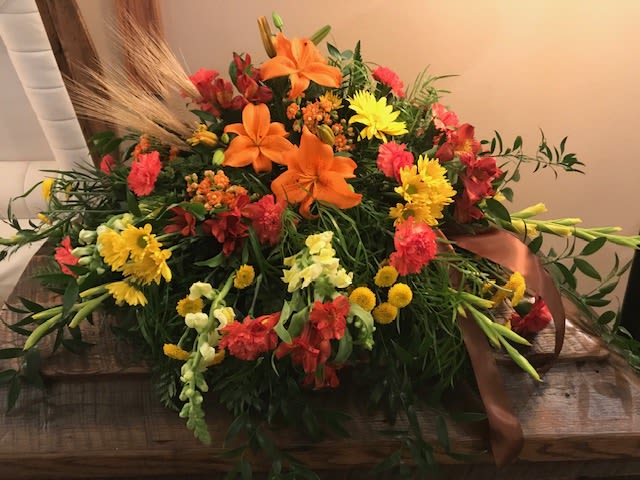 Autumn Memories Casket Spray - The Autumn Memories Casket Spray captures the warmth and richness of the season in a heartfelt tribute. Featuring brilliant orange lilies, golden chrysanthemums, orange carnations, yellow daisies, yellow button poms, yellow snapdragons, orange alstroemeria, this spray glows with the colors of fall. Accented with wheat, lush greenery, it beautifully symbolizes gratitude, harvest, and the cycle of life. 