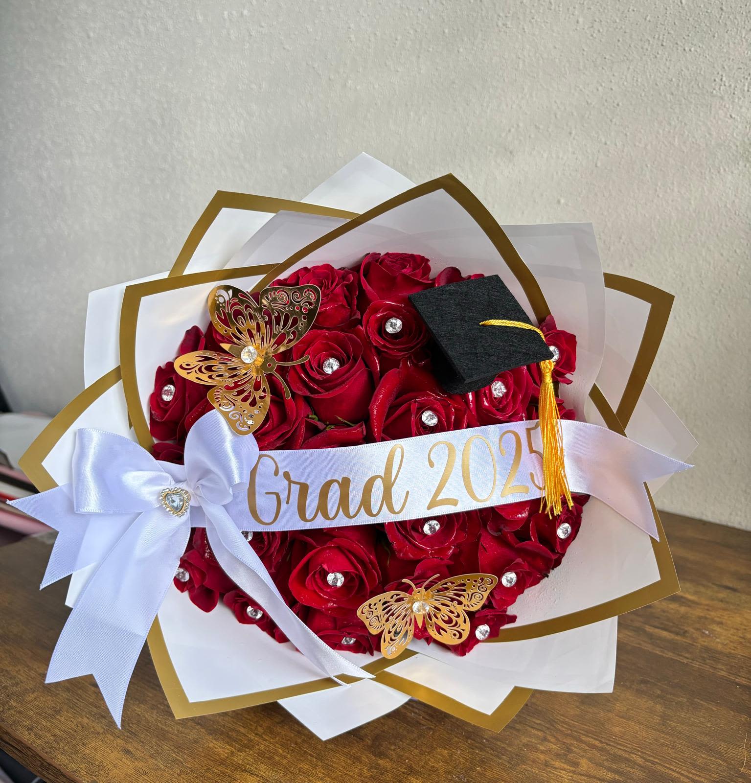 Graduation Bouquet 2025 / Ramo de Graduación 2025 - Graduation Bouquet 2025 / Ramo de Graduación 2025  Celebrate success in style with our Graduation Bouquet 2025, featuring luxurious red roses adorned with crystal accents, golden butterflies, and a mini graduation cap. Wrapped in elegant white and gold paper with a custom “Grad 2025” ribbon, this bouquet is the perfect way to honor hard work and new beginnings.  Celebra el éxito con estilo con nuestro Ramo de Graduación 2025, elaborado con elegantes rosas rojas decoradas con cristales, mariposas doradas y un pequeño birrete de graduación. Envuelto en papel blanco y dorado con cinta personalizada “Grad 2025”, es el detalle ideal para reconocer logros y nuevos comienzos.  Perfect for / Perfecto para: Graduation celebrations and milestone achievements. Includes / Incluye: Fresh red roses, gold and white wrapping, butterflies, crystal accents, and ribbon. Note / Nota: Custom text available upon request.