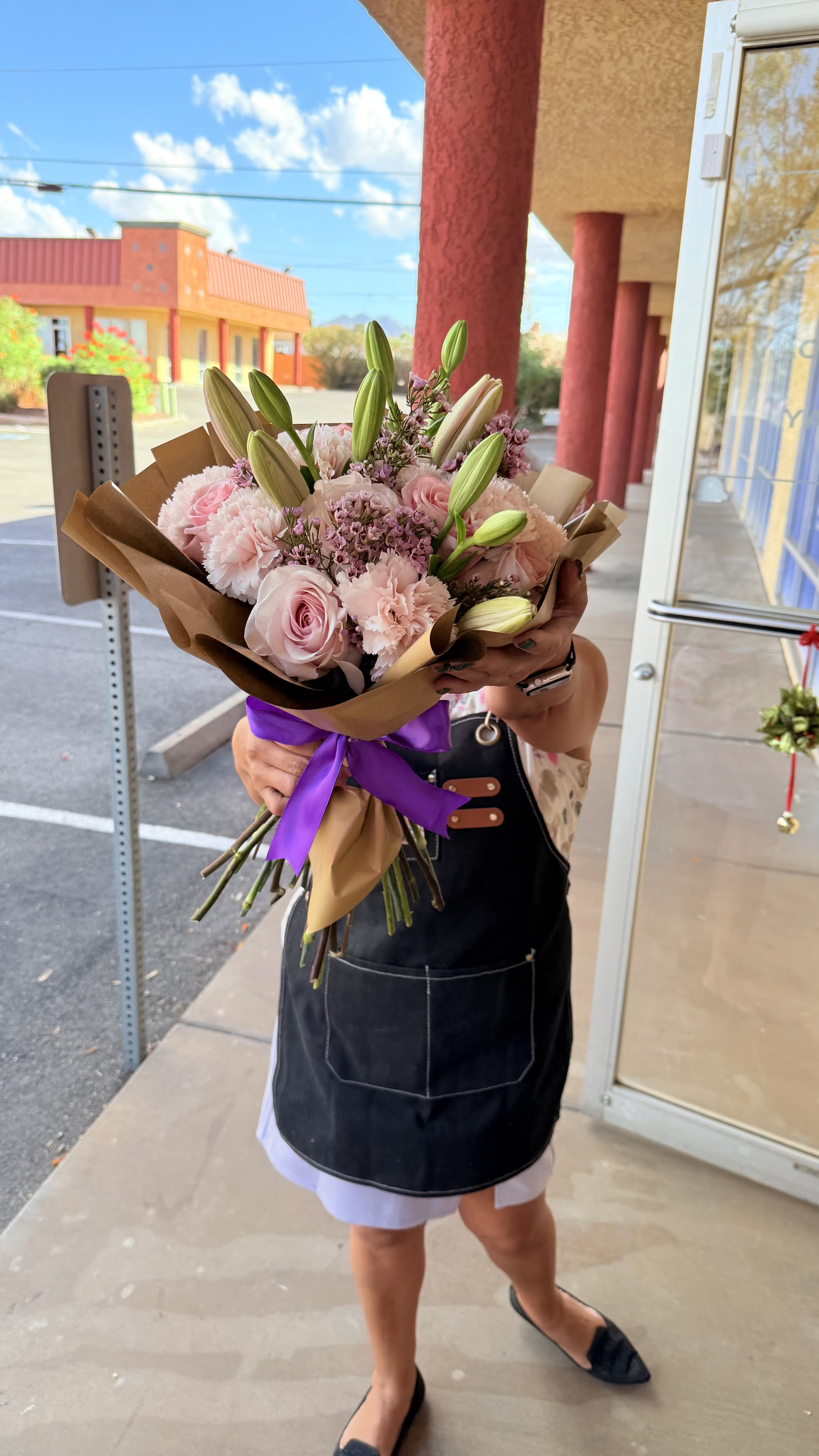 Blushing Elegance  - Soft. Romantic, and effortless chic capture the heart of love in every  petal. This hand tide bouquet features a dreamy  mix of blush rose pink, pink carnations, lilies, and delicate wax flowers, wrapped in rich Kraft paper and finished with a luxurious purple satin ribbon - the signature of A Touch of Flowers Boutique.