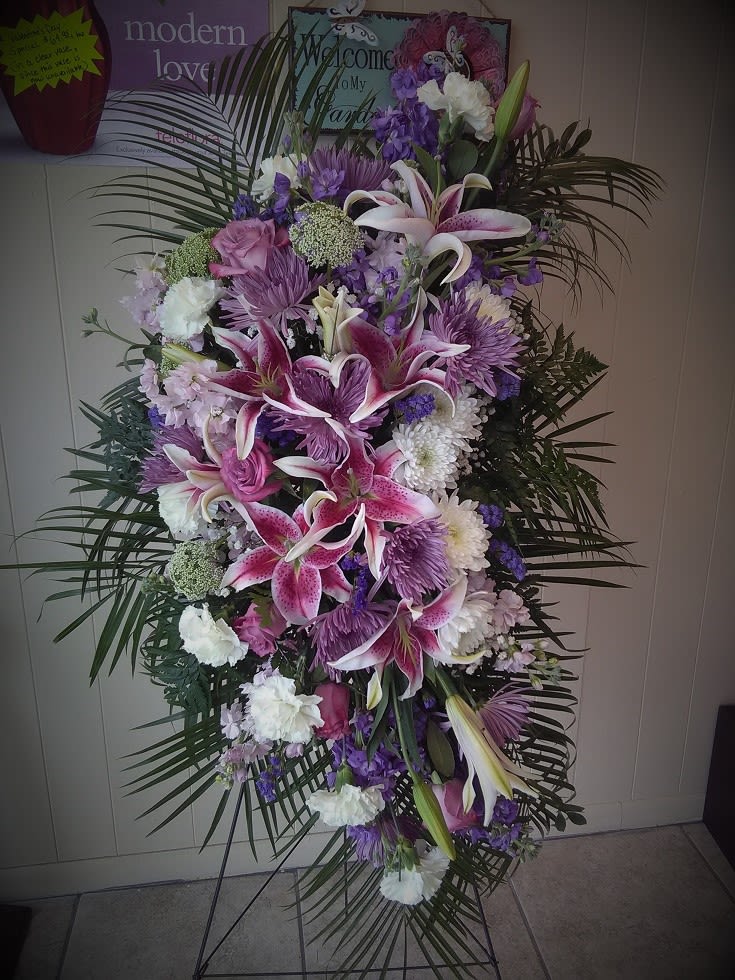 Stargazer's Spray - An eclectic mix of pinks and purples makes this standing spray different from all the rest!  The aroma of stargazer lilies and stock and will fill the air, leaving feelings of serenity and joy for the passing of your loved one.   Placed on an easel, the recipe for this standing spray consists of stargazer lilies, lavender roses, queen anne's lace, stock, carnations, and numerous kinds of mums, making it one of our favorites. What started off as a designer's choice, ended up being an in-house favorite, for looks and value.      This spray stands over 3 feet tall (not including the easel).
