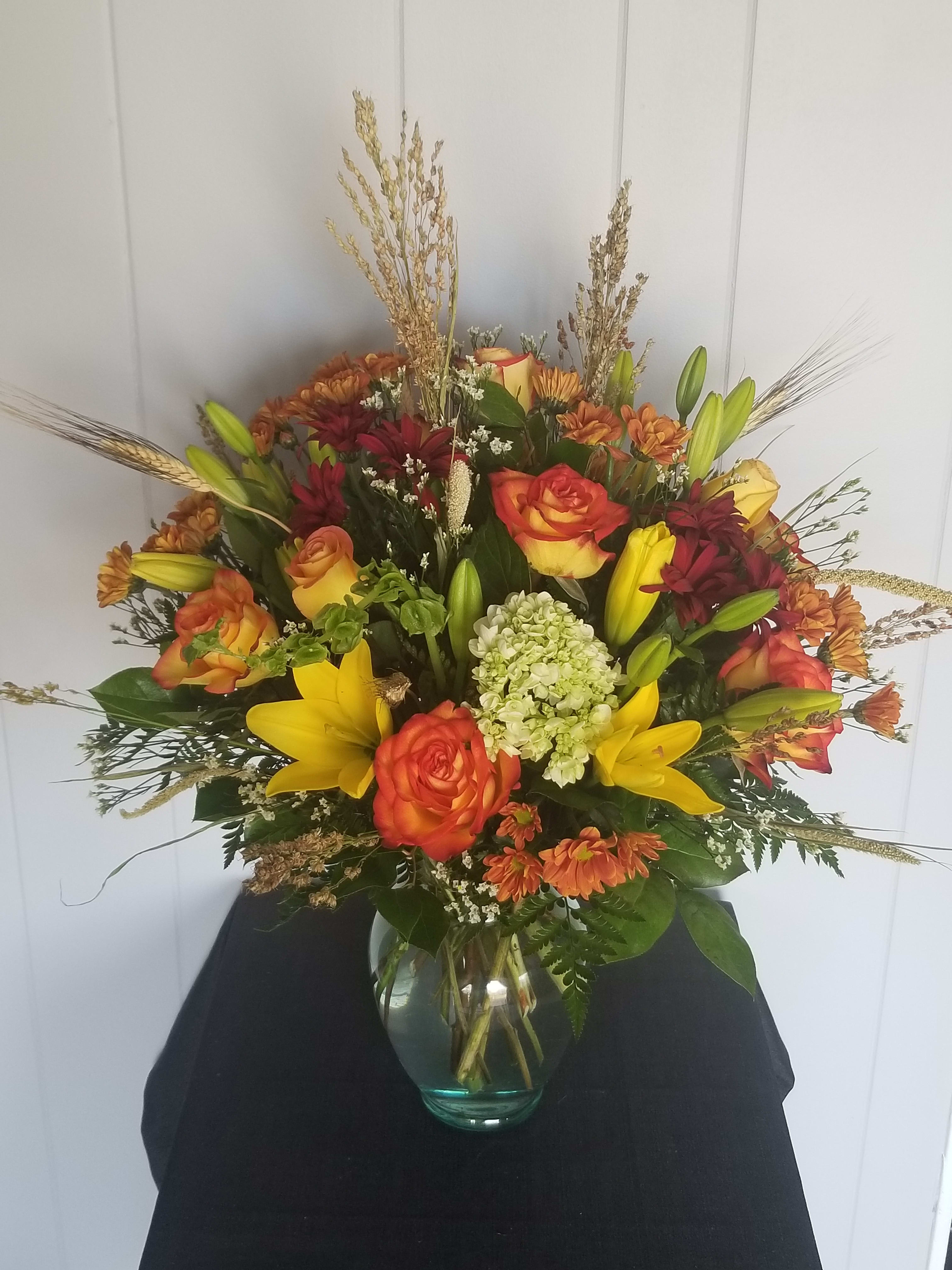 A Elegant Fall Arrangement  - A custom arrangement of rich fall flowers, in the tones of  orange, yellow, and burgundy. This elegant arrangement contains Roses, Lilies, mums, seasonal Hydrangea surrounded by lush greens and fall filler.   