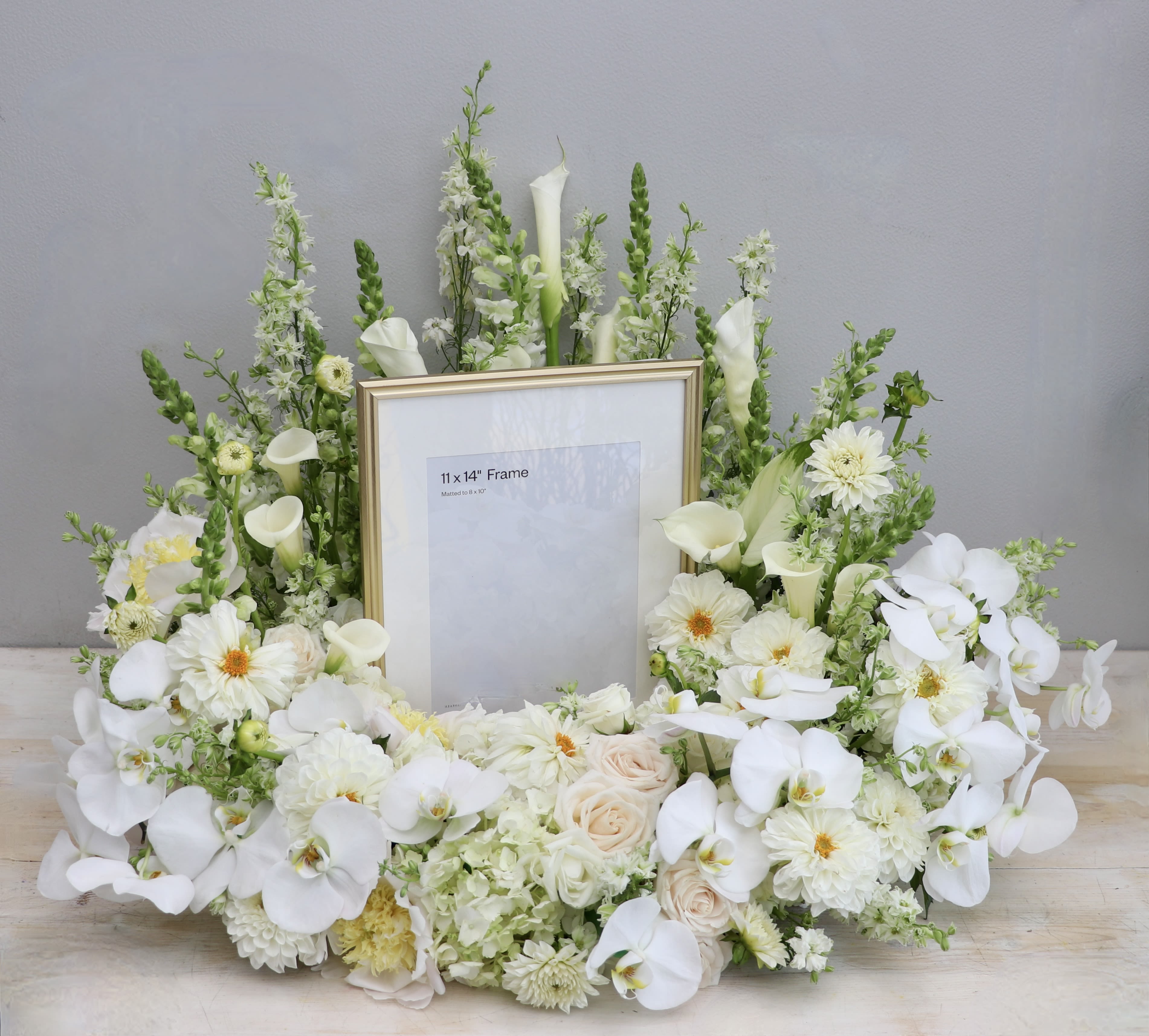 White Frame Wreath  - This urn tribute wreath includes a mix of orchids, roses, and seasonal greens. This urn wreath is made with greens and whites but you may request other colors in the special instructions during checkout.  Standard size is 20'', deluxe is 26'' and premium is 32''. Interior diameter is about 10'' for standard size. (Frames are placed for display - not included)