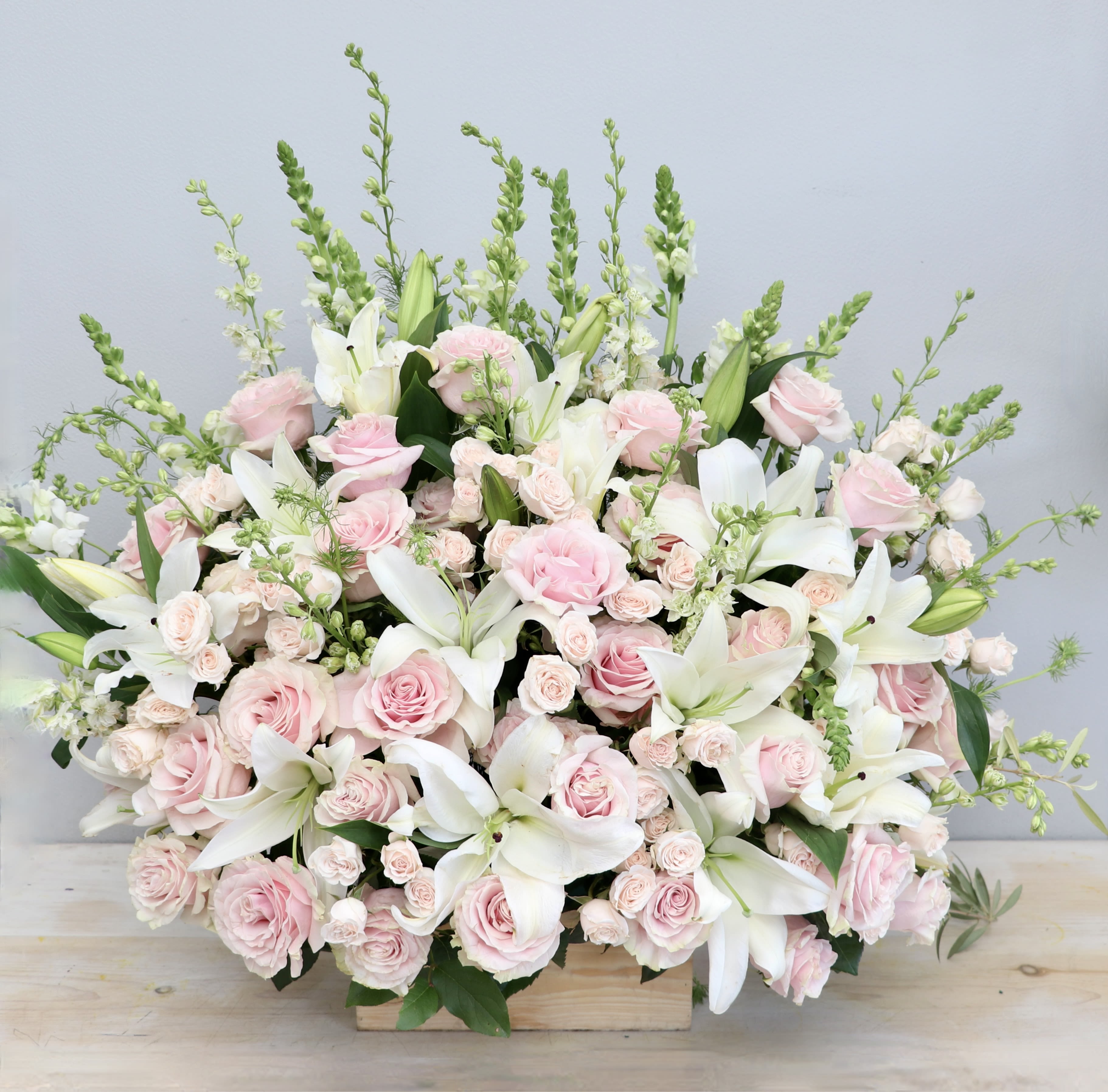 Lily &amp; Pink Love - This sympathy arrangements combines soft pink roses with fragrant white lilies. Snaps, larkspur, and spray rose are also added to this lovely podium piece. 