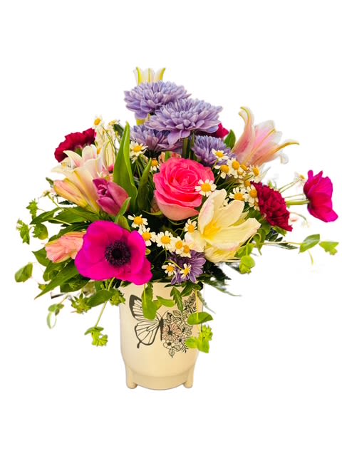 Butterfly Garden Bouquet -  A charming medley of bright and cheerful blooms, the Butterfly Garden Bouquet brings the beauty of nature indoors. Featuring vibrant roses, lilies, mums, carnations, and daisies in a delightful mix of pink, yellow, purple, and white, this arrangement radiates joy and warmth. Displayed in a keepsake cream ceramic vase adorned with a graceful butterfly design, it’s the perfect gift to celebrate spring, friendship, or simply brighten someone’s day.