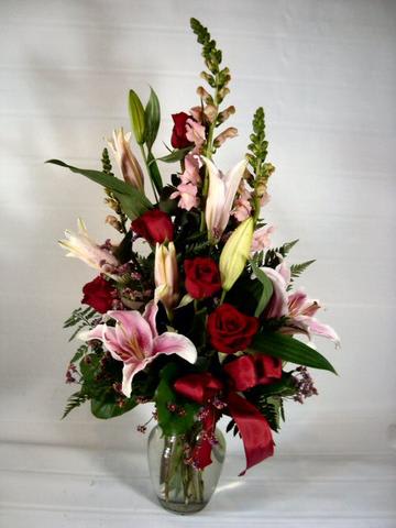 All you need is love - Stargazer lilies , pink snapdragons ,red roses and filler in a  c red or clear glass vase container.