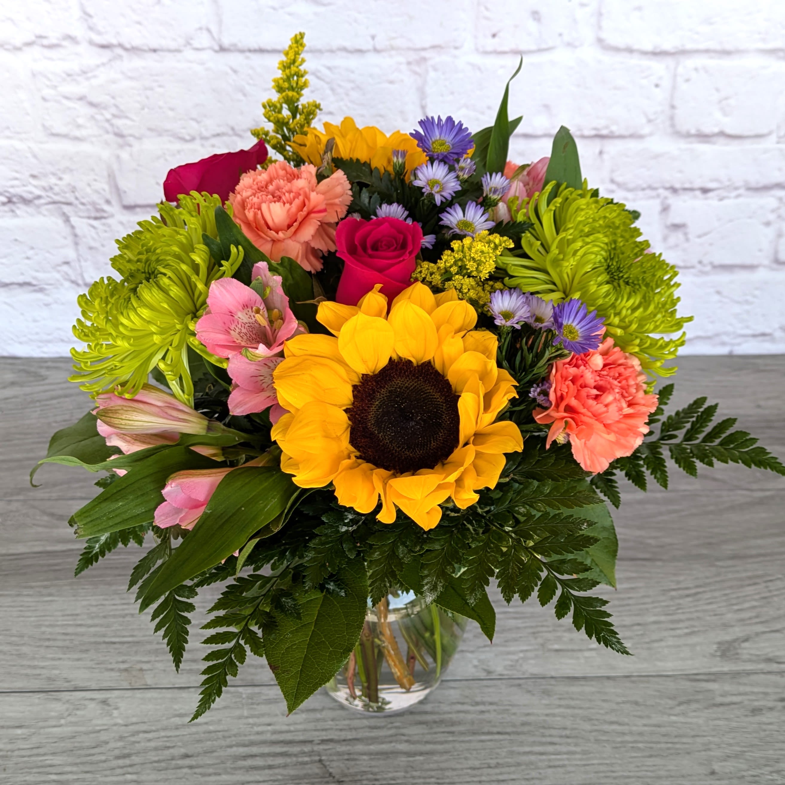 Mountain Meadow - Mountain Meadow consists of sunflowers, alstroemeria, roses, spider mums, carnations, solidago, and monte casino, modestly arranged in a 7” rose vase.  All Around Orientation 13”H X 12&quot;W 