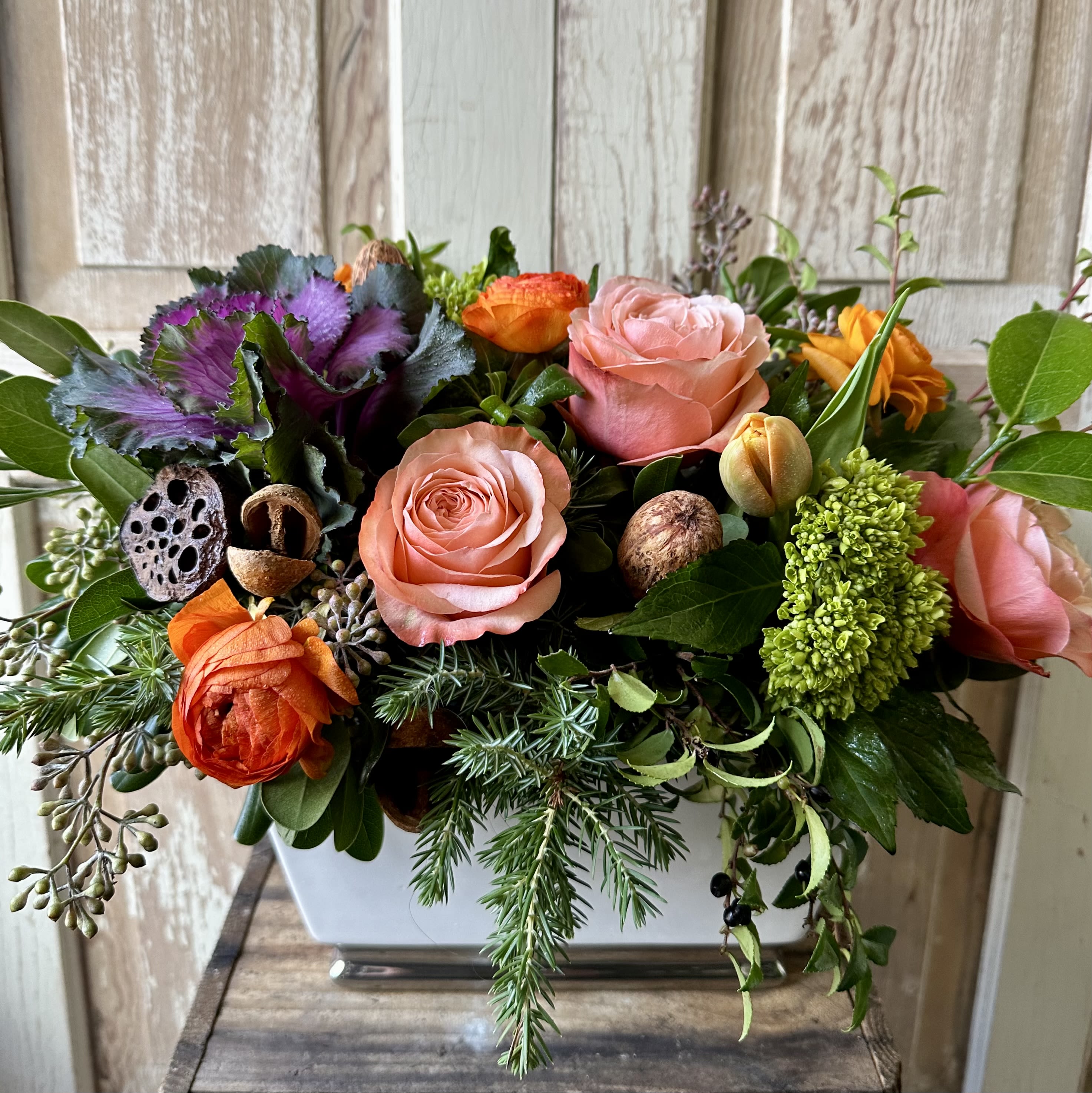 Give Thanks  - A seasonal display of kale, two toned orange roses, ranunculus and natural accents. Dimensions for this arrangement are 14” x 10”.