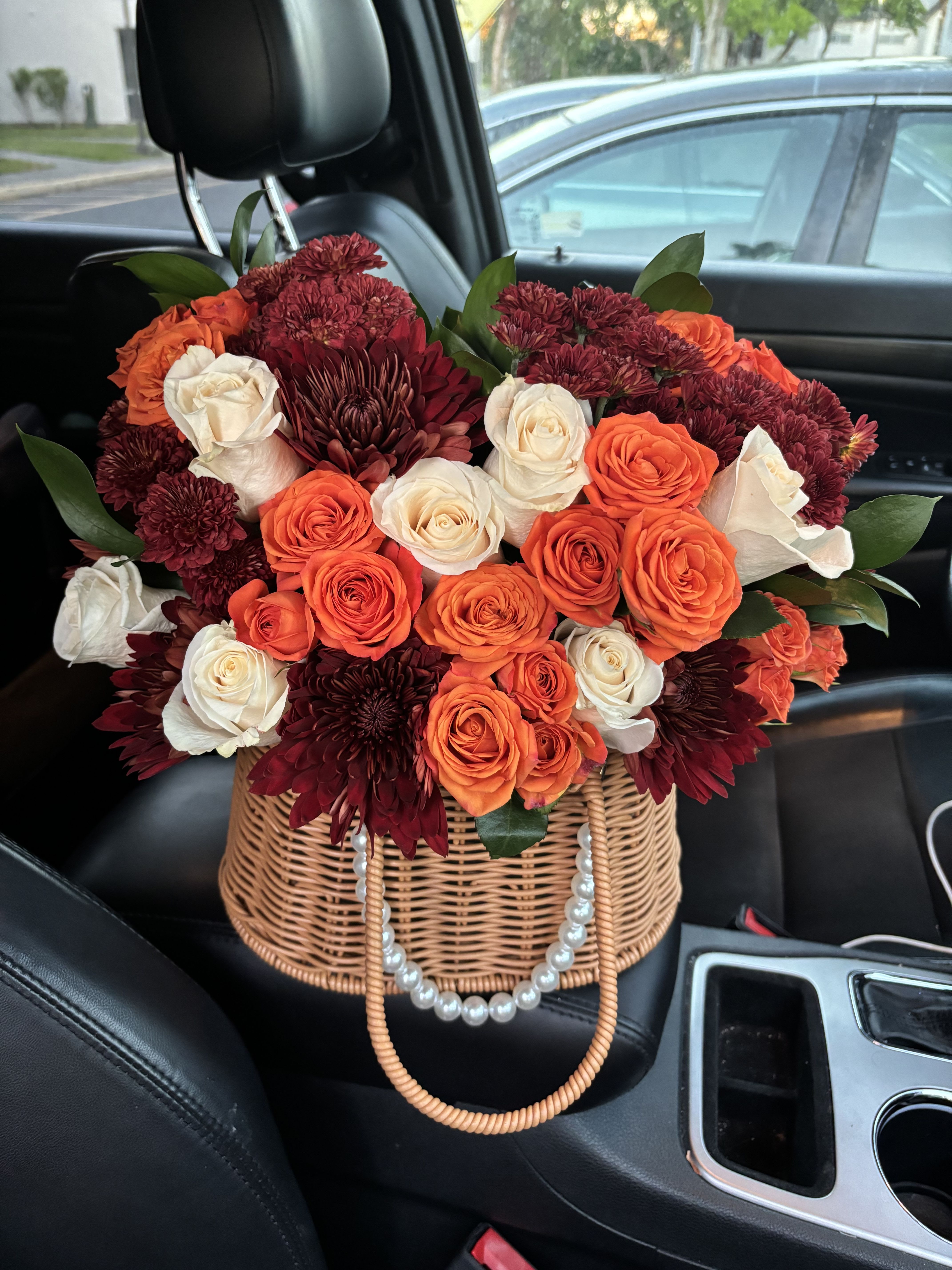 Autumn Basket Arrangement - Bring the warm charm of fall to any occasion with this stunning basket arrangement. Designed in a woven handbag-style basket with elegant pearl detailing, it features a rich blend of orange and cream roses paired with deep burgundy chrysanthemums. Perfect for birthdays, fall celebrations, thank-you gifts or to brighten someone’s day with cozy autumn vibes.  Llama la atención con este adorable arreglo en canasta estilo bolso con detalle de perlas, ideal para dar un toque cálido y elegante. Incluye una hermosa combinación de rosas naranja y crema junto con crisantemos en tonos borgoña que evocan la esencia del otoño. Perfecto para cumpleaños, celebraciones otoñales, agradecimientos o para sorprender con belleza de temporada.   Aprox. 28–35 tallos  Ideal como regalo de temporada o decoración de hogar Flowers may vary slightly depending on availability / Sujeto a disponibilidad de flores