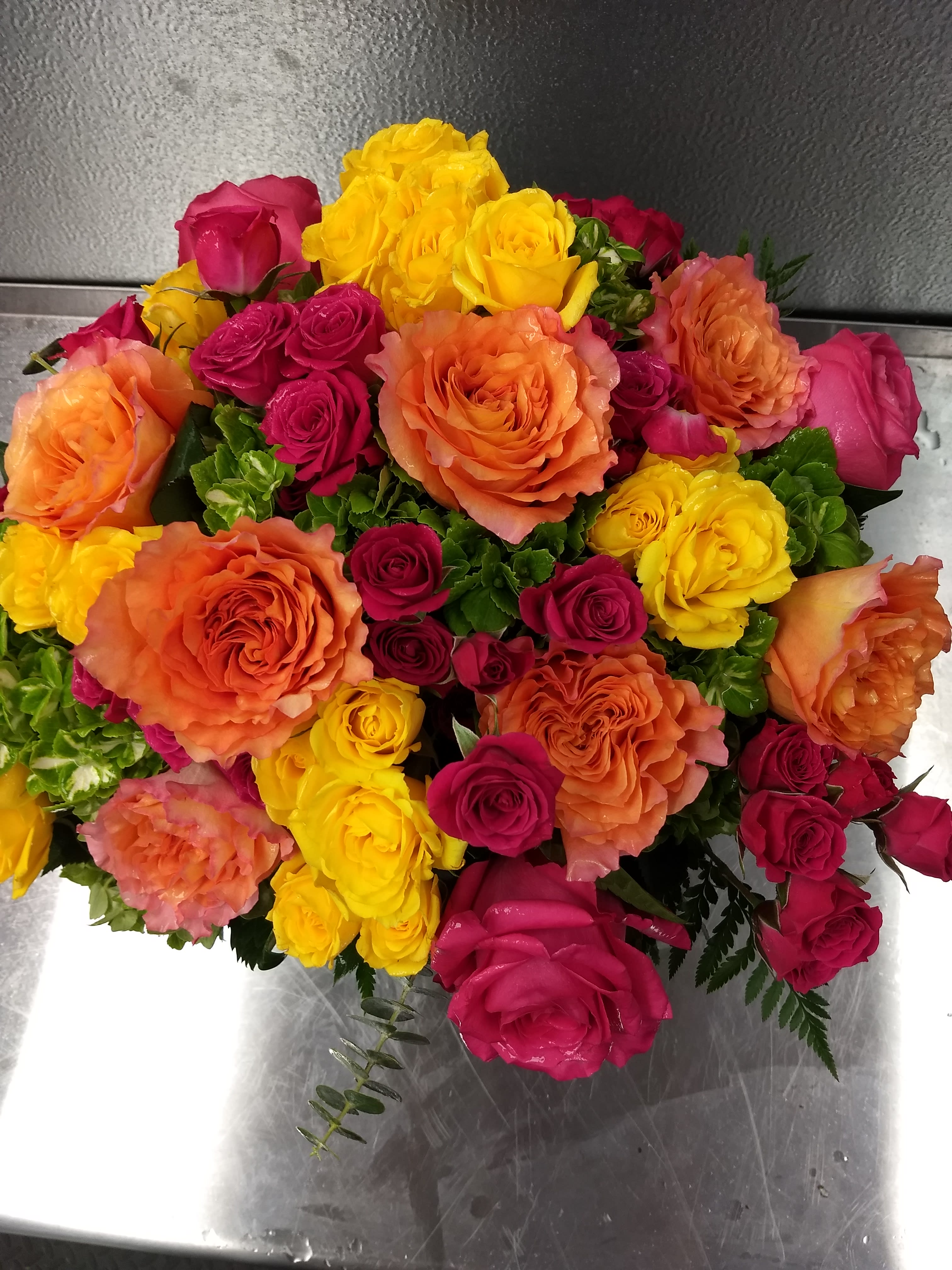 Blossoms in Vogue Blossoms in Vogue - Blossoms in Vogue A vibrant symphony of color and life—brilliant green hydrangeas dance with fiery hot pink and bi-color roses, while playful spray roses in hot pink and sunshine yellow whisper secrets of summer. Cradled in a vase lined with emerald leaves, this bouquet is not just a gift, but a radiant poem of nature’s finest hues.  Approximately 13" W x 12" H  Orientation: All-Around      As Shown : T74-1A     Deluxe : T74-1B     Premium : T74-1C