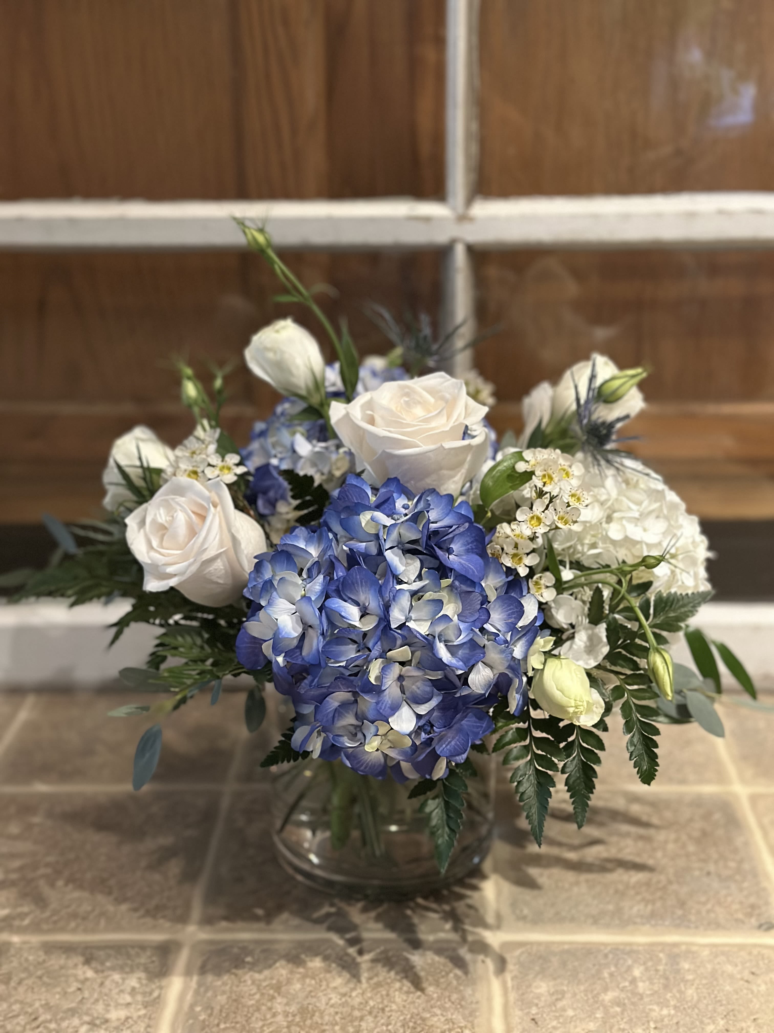 By The Cape - Bringing coastal charm inland with classic blue and white. Arrangement will include blue and white hydrangea, white roses, and white lisianthus. 