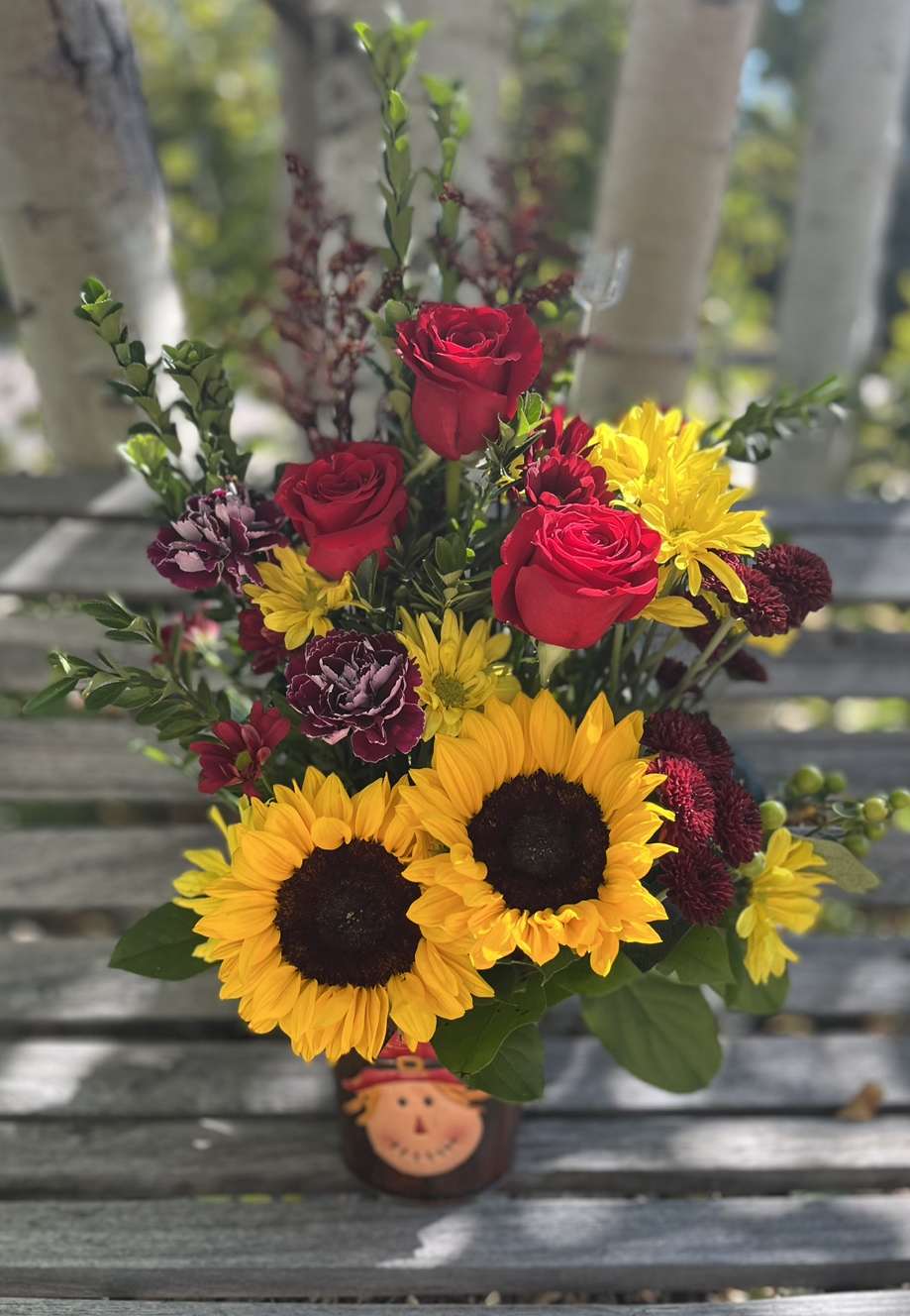 Scarecrow* Autumn - This cute tin scarecrow* pot is filled with fall flowers and greens. Perfect novelty arrangement for everyone who loves Autumn!  *Scarecrow available while supplies last. May have owl or sunflower on pot once scarecrows are gone. 