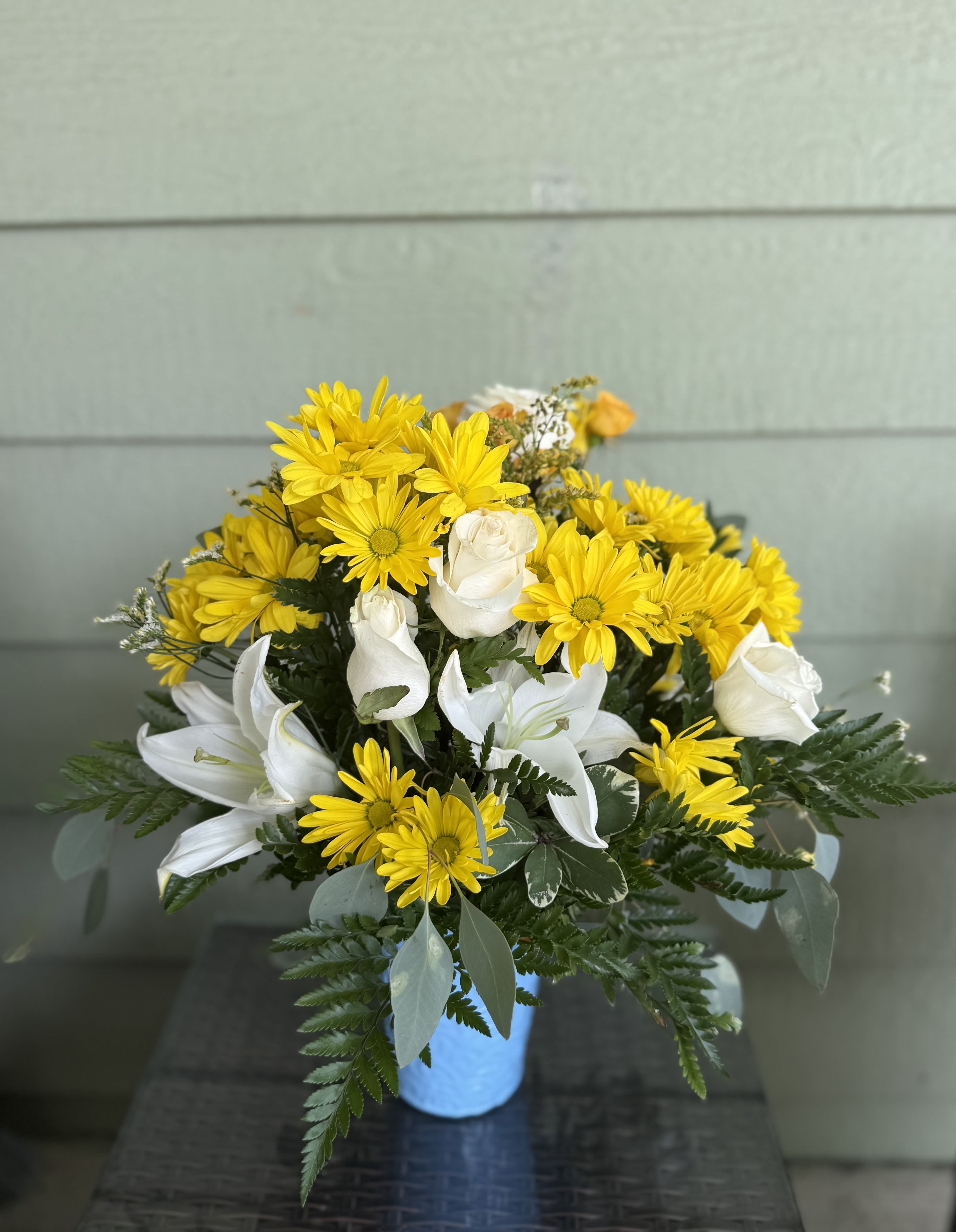 Welcome Little One – Baby Boy  - Celebrate the arrival of a precious baby boy with this charming and cheerful flower arrangement. Designed in soft shades of blue, white, and yellow, it features fresh seasonal blooms like fragrant white lilies, white roses, and yellow daisies. Accented with lush greenery and arranged in a castle blue or green container, this arrangement is a heartwarming way to send your love and congratulations to the new parents. A beautiful gift that symbolizes new beginnings, joy, and the boundless love a little boy brings into the world.