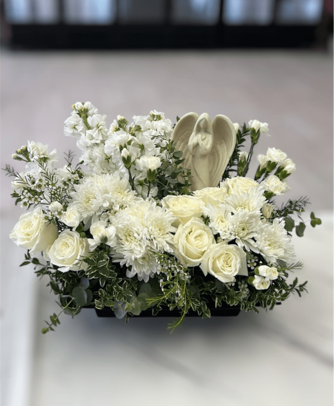 All White Funeral Centerpiece - Please note that florists may need to make substitutions based on inventory to ensure the freshest blooms are delivered, while maintaining the arrangement's overall aesthetic.