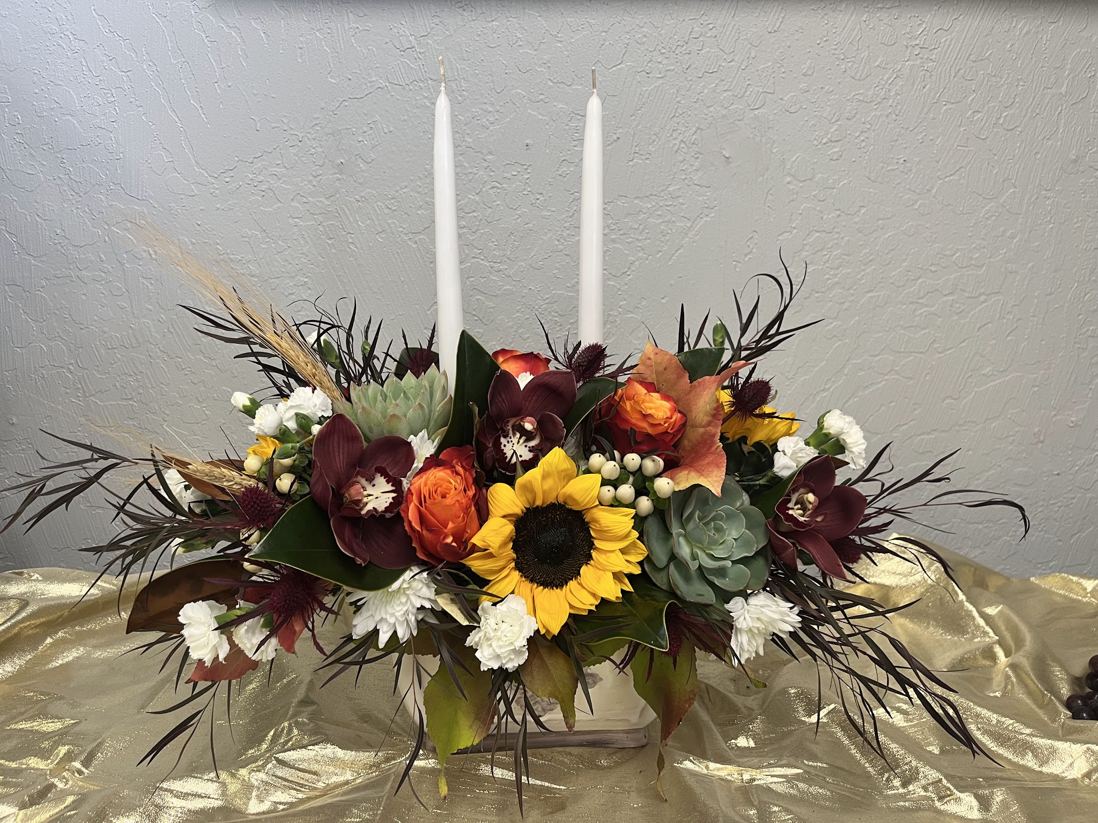 Elegant Centerpiece - An elegant centerpiece for your holidays with friends and family. Crafted by our artisan florists, it’s filled with a gathering of fresh-picked blooms in brilliant colors and finished with an orange candle to warm hearts and homes.