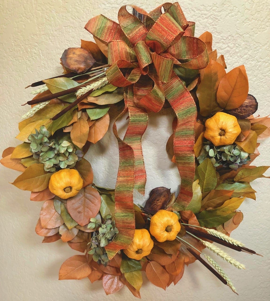 Seasonal Preserved Autumn Wreath - This beautiful wreath is hand-decorated by our OBF designers to bring out the best of the Autumn warm fuzzies-- and since it's preserved and dried it will last you many Autumns! Featuring preserved and dried flowers and leaves, including yarrow, hydrangea, pods, and cattails. Additional decoration will include a fabulous seasonal bow and raffia mini pumpkins (all dependent on availability).   Base wreath measures 18&quot; across. ** Call us if you'd like to have this shipped anywhere in the U.S. 805-492-2206