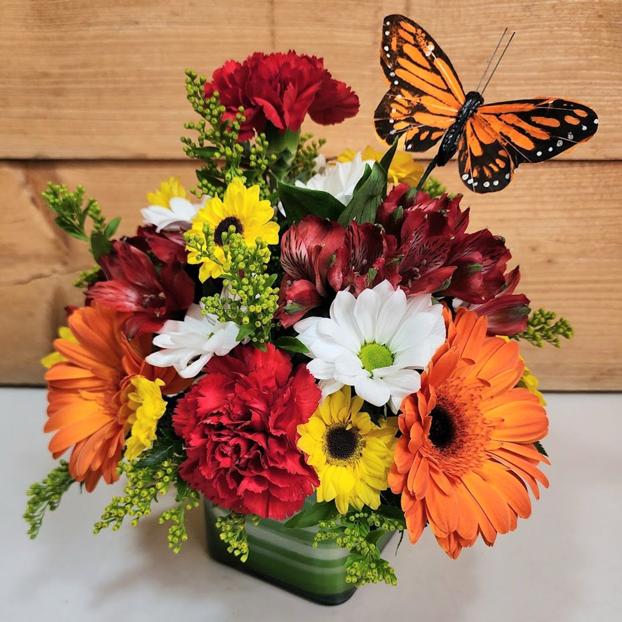 Bright Beauty Butterfly Cube Bright Beauty Butterfly Cube - The Bright Beauty Butterfly Cube is a wonderful presentation of Carnations, Mini Carns and a butterfly pick highlighted by daisies, yellow vikings and orange alstroemeria all featured in a glass cube.  Approx 10" H x 10" W  PLEASE NOTE: Some flowers, vases and other products pictured are subject to availability, and may be substituted for a similar item if unavailable according to our substitution policy.