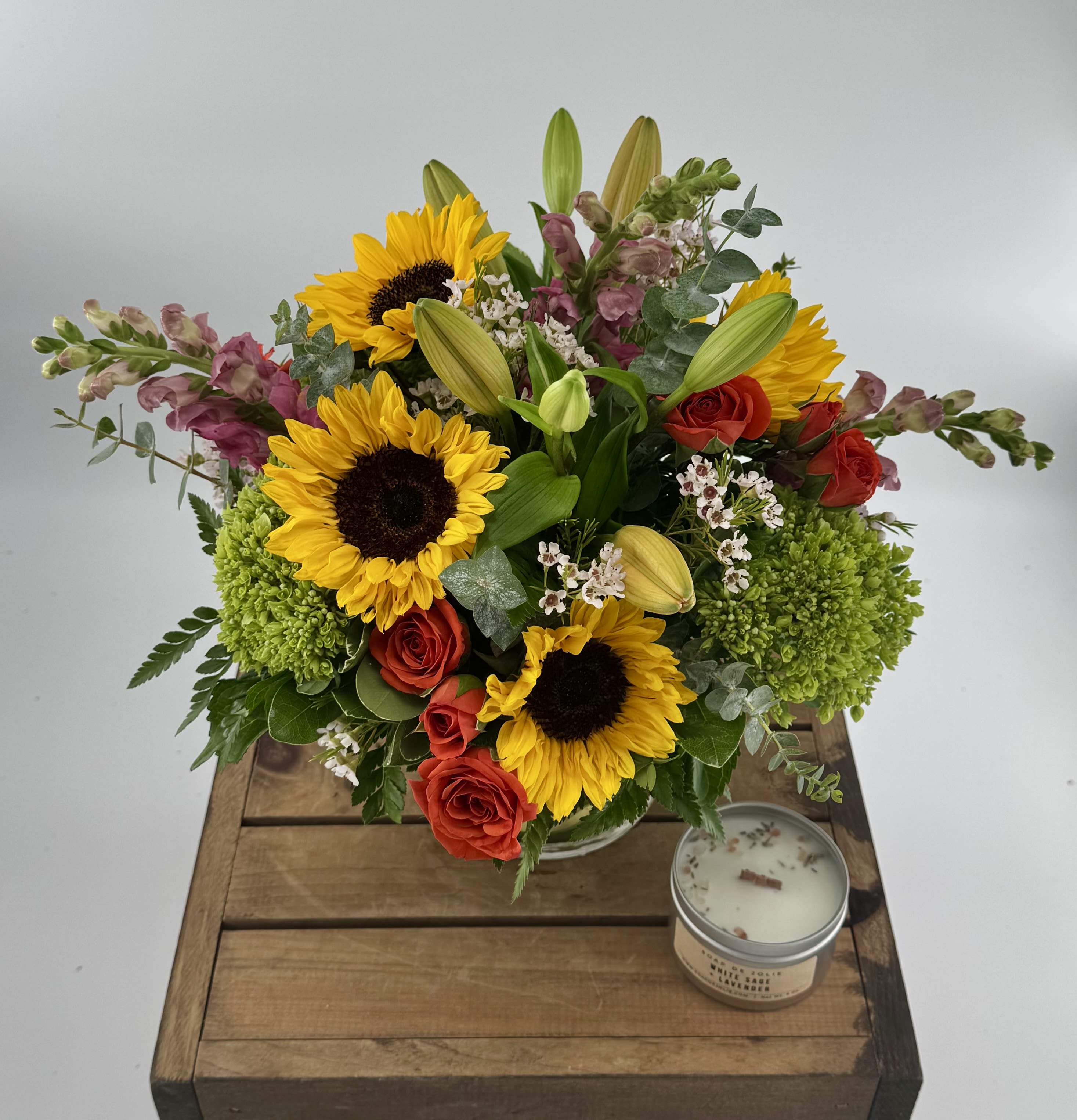 Citrus Splash (DB) - Introducing a breathtaking flower arrangement that is as vibrant as it is elegant. This stunning composition beautifully combines hydrangeas, spray roses, sunflowers, waxflower, eucalyptus and lilies in a leaf-lined glass vase, creating a captivating display of natural beauty.   