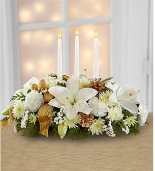 The Seasons Glow - The Season's Glow centerpiece blooms with winter elegance and holiday enchantment to grace your Christmas celebrations. White LA hybrid lilies, carnations, chrysanthemums and statice are arranged amongst holiday greens and accented with gold pine cones and a gold plaid French wired ribbon for an exquisite look. Arranged to encircle 2 to 3 white taper candles, this stunning arrangement will bring a sweet sophistication to your holiday festivities. This centerpiece is approximately 7&quot;H x 21&quot;W. SHOWN PICTURE IS THE MED.SIZE. Smaller size has 2 candles. Your purchase includes a complimentary personalized gift message.