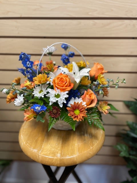 Autumn Rain Autumn Rain - Mixed cut flowers with daisies, delphinium, orange roses, and white lilies in a white basket.