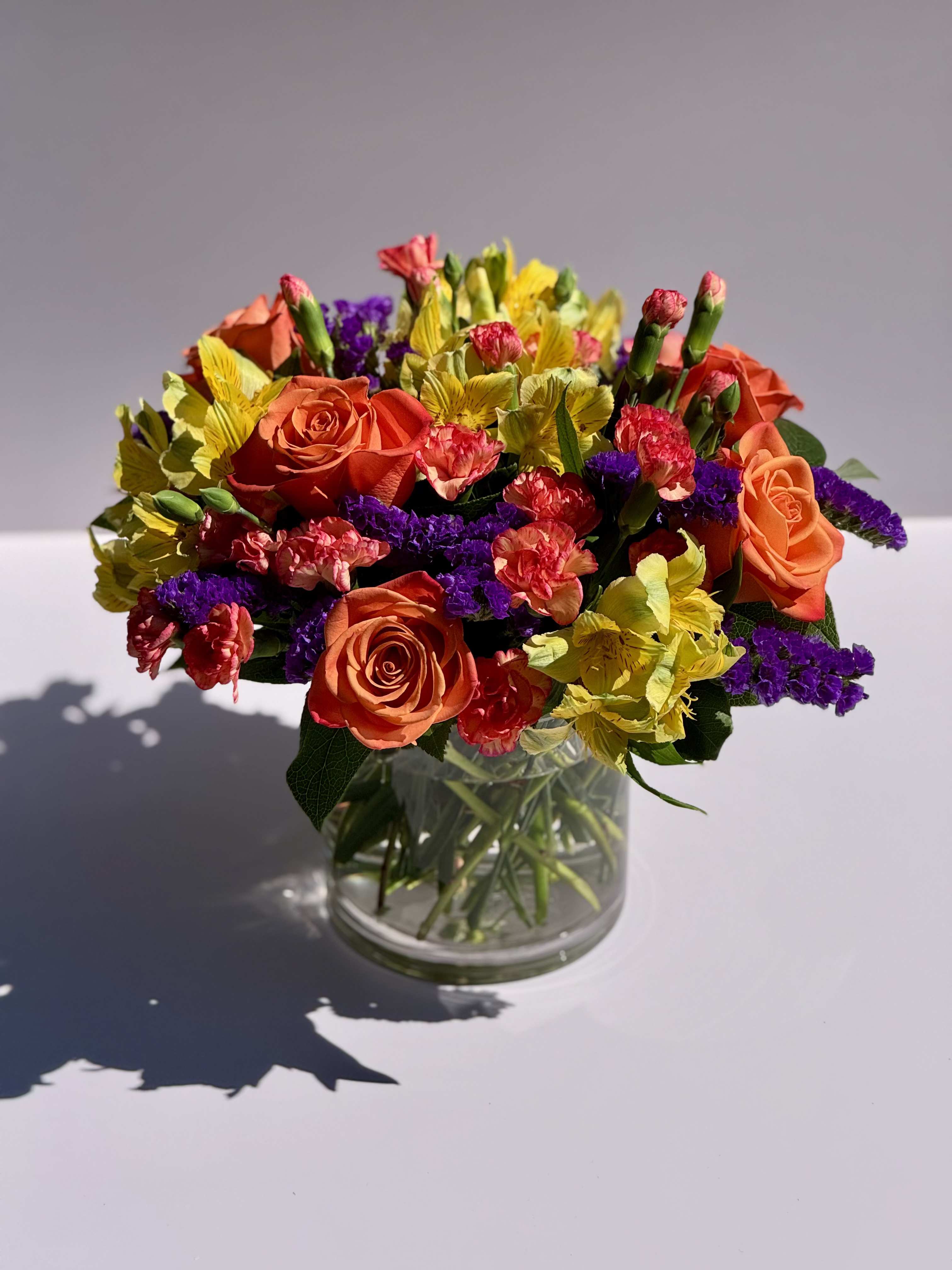 Just Because Just Because - Vibrant orange roses accented with mini carnations, alstroemeria, purple statice, and lemon leaf.  Overall size: 9" x 9"