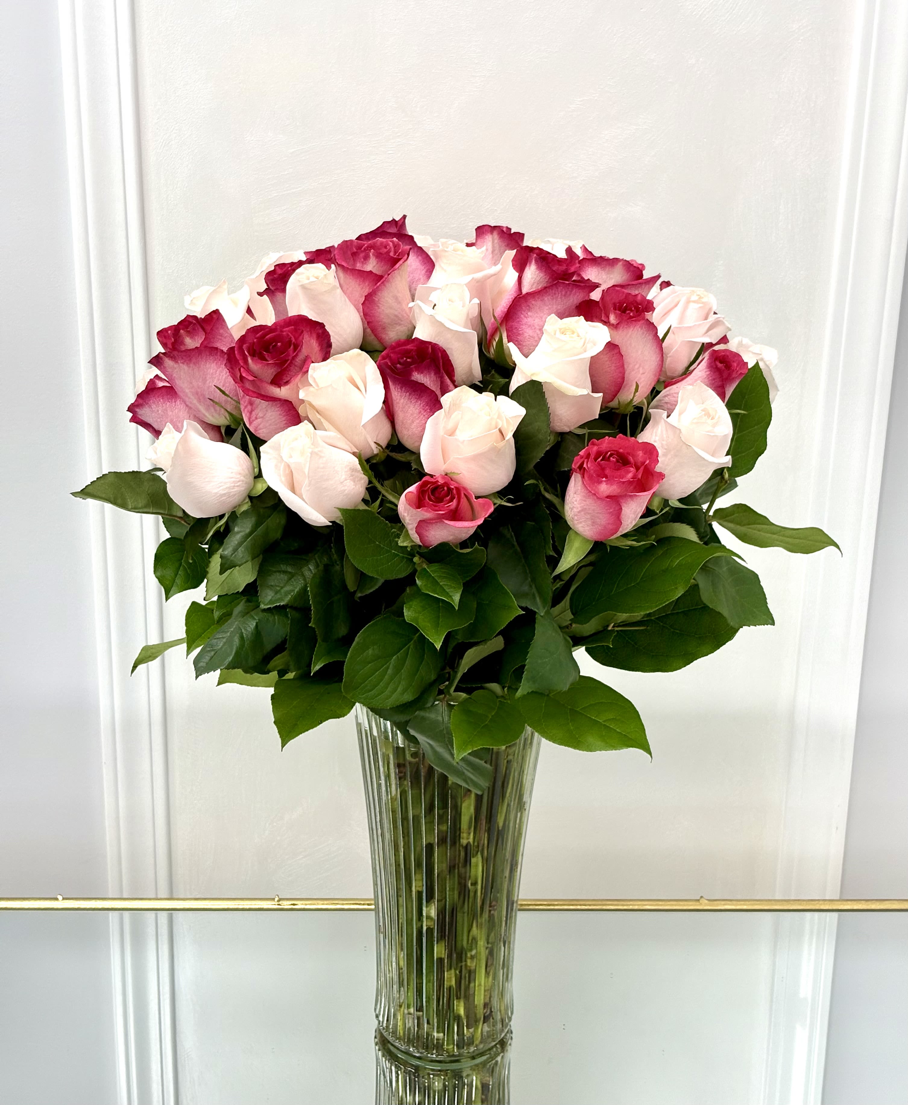 Rose Symphony By VLM Flowers - A romantic harmony of soft blush and vibrant fuchsia roses, Rose Symphony is a graceful composition that celebrates beauty in every shade. Arranged in a tall glass vase with lush green foliage, this bouquet is a perfect serenade for love, gratitude, or celebration.