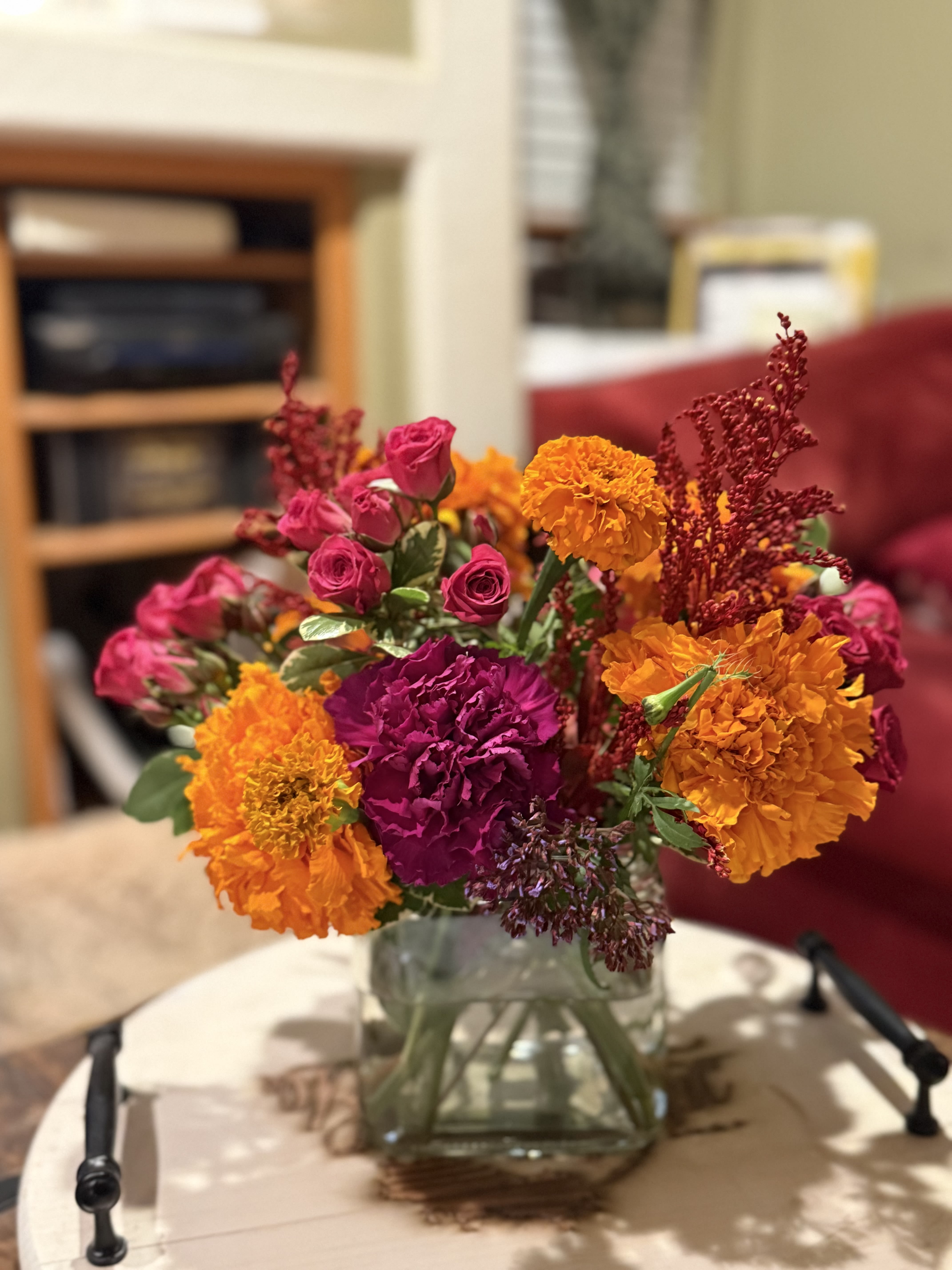 Marigold Designers Choice - Send and arrangement filled with Orange marigolds complimented with other fall colored flowers to brighten someone’s day! The recipient will be able to enjoy the fragrant blooms and brighten up their space with a pop of color.  *** The photo is an example but due to high demand, the bouquet delivered may not have the flowers or all  of the shades of orange, magentas and reds  included in the listing photo.**** Everything is blooming orange, purple, and red! We have so many spectacular things we can’t possibly put them all on the website. Pick a designers choice and we will pick the most fabulous design for you!  *****Florist choice of container will be either a clear vase, white metal pot or box.