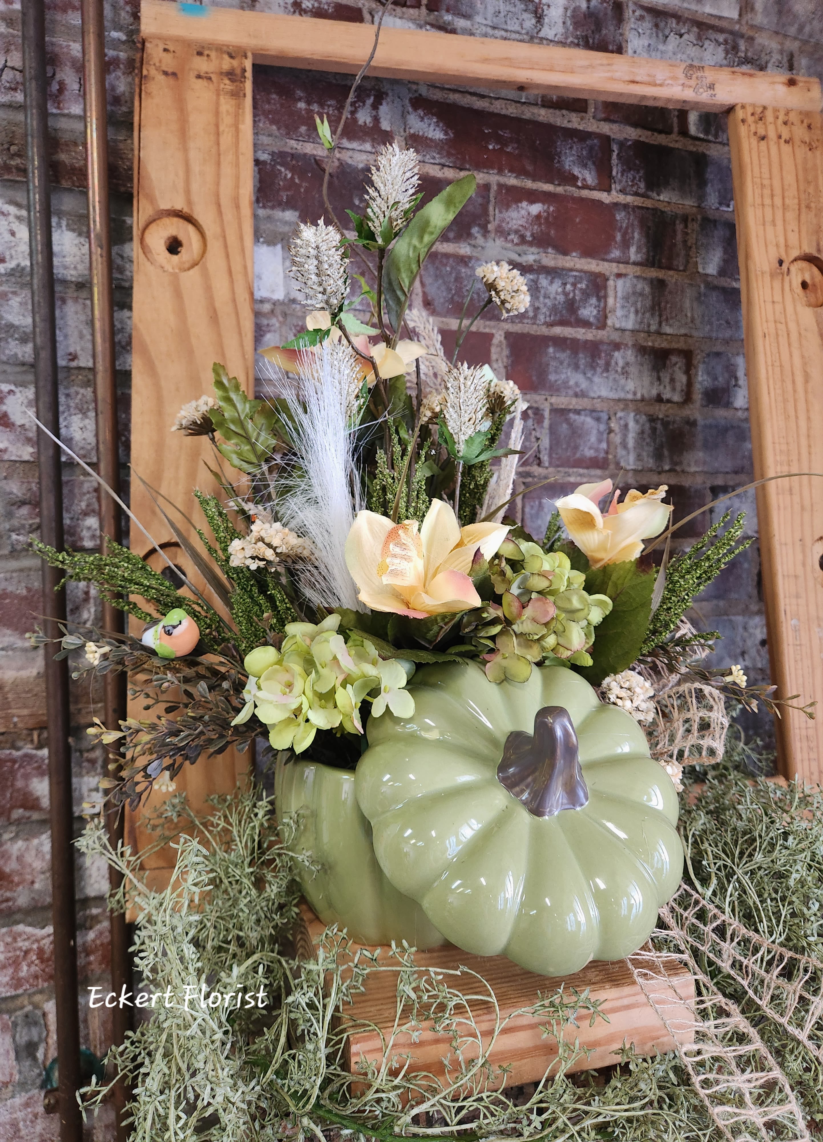 Eckert Florist's Permanent Botanical Green Pumpkin *LOCAL DELIVERY ONLY  - This green ceramic pumpkin is filled with artificial neutral colored flowers and greens. A non-typical autumn choice for that someone special or for your own decor. *Flowers and colors may vary.