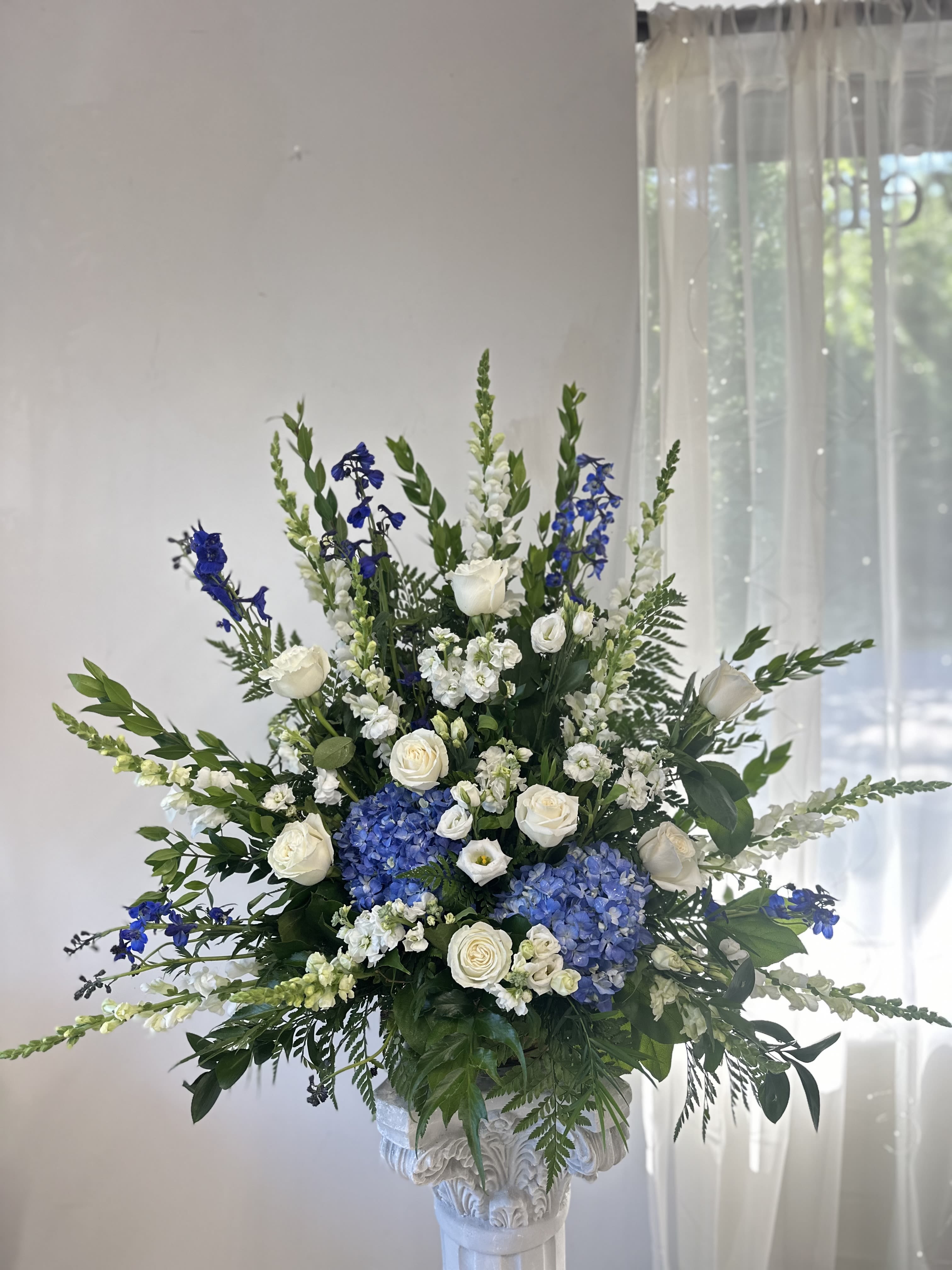 Ocean of Memories Basket by Westford Florist Art by Veny - A serene tribute to cherished moments, the Ocean of Memories One Sided Basket by Westford Florist Art by Veny beautifully encapsulates the essence of remembrance and comfort. This exquisite arrangement features soft blue delphiniums mingling harmoniously with elegant white stock, lissianthus, snapdragons, and roses, all cradled within lush blue hydrangeas. Perfect for expressing heartfelt condolences or honoring a loved one’s legacy, this thoughtful sympathy basket serves as a poignant reminder that love transcends even the deepest sorrow. Ideal for any memorial setting or home display, it offers solace in times of need while celebrating the beauty found in memories shared.