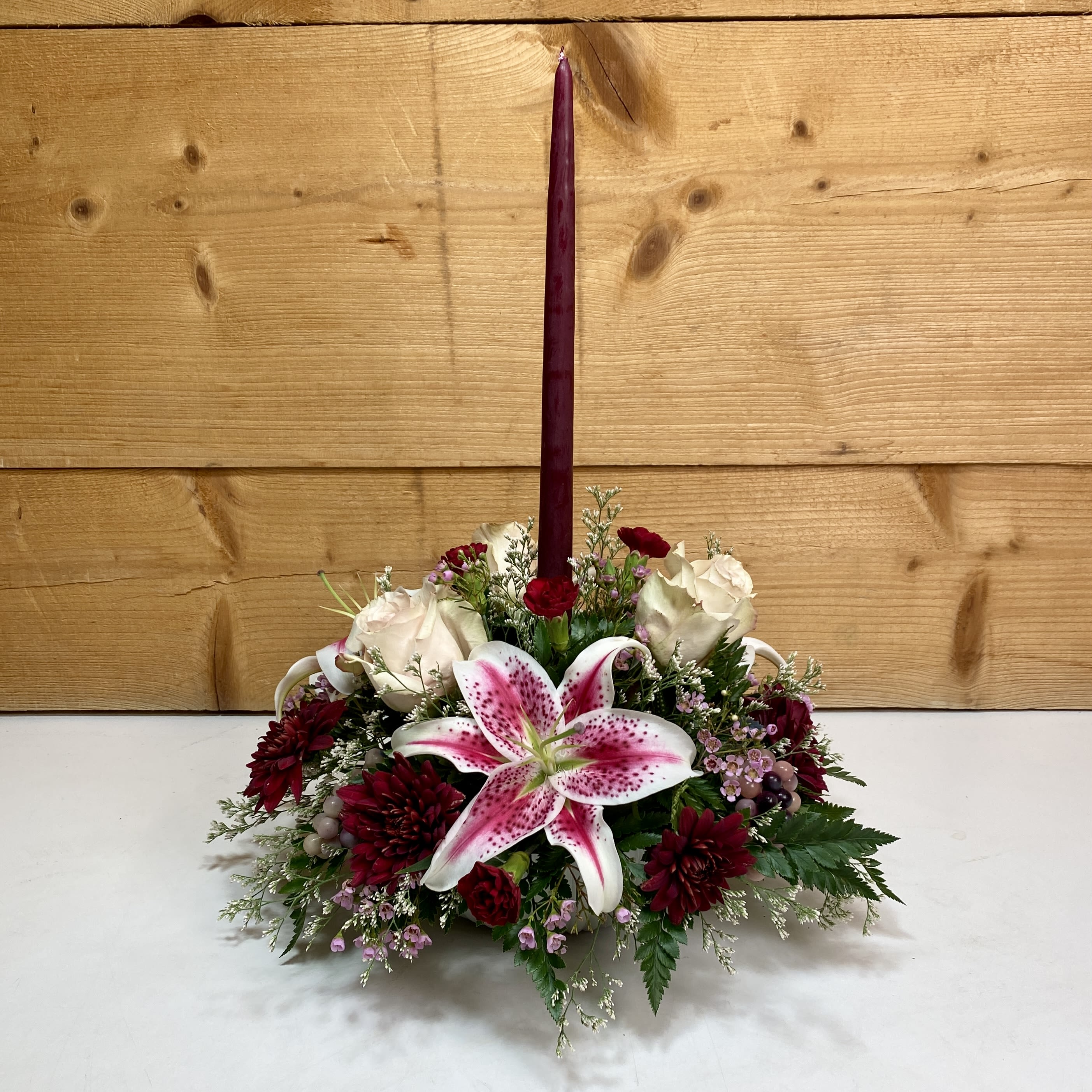 Merlot Memories - Merlot Memories is the perfect floral arrangement for your Thanksgiving festivities, featuring burgundy flowers like mini carnations and pom poms, along with quicksand roses. Presented in a low, ribbed bowl adorned with artificial grapes and a 15&quot; burgundy candle, this arrangement would make a beautiful gift to give thanks this season, or to decorate your own home.  Approx. 15&quot;x20&quot;