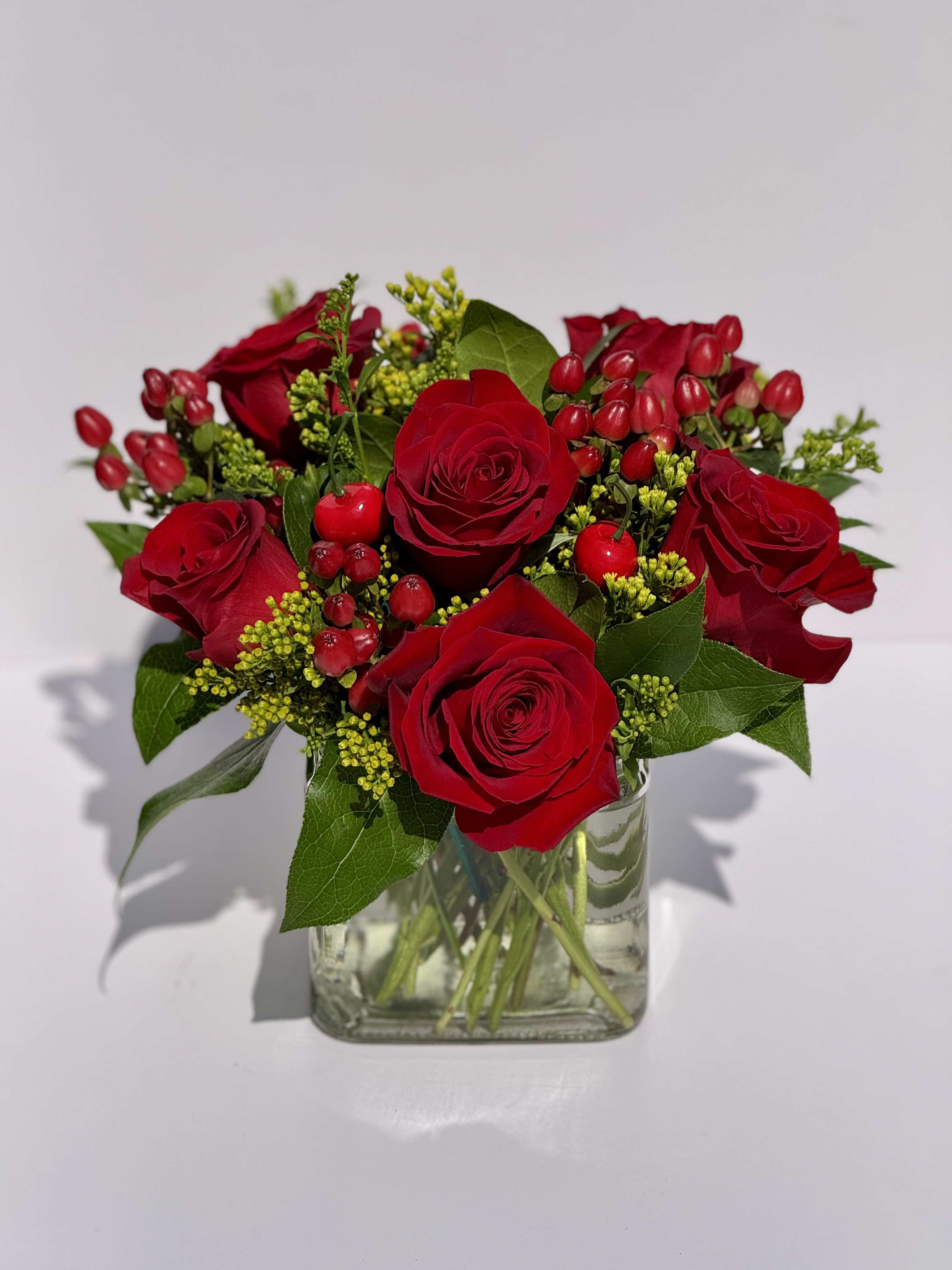 Red Ruby Red Ruby - A bold and romantic mix designed to captivate at first glance. Red Ruby features velvety red Freedom roses paired with deep red hypericum berries, bright golden solidago, and lush greenery for texture and warmth. Finished with delicate faux cherry stems for a touch of whimsy, this design embodies passion, confidence, and charm — all in one breathtaking bouquet. Perfect for anniversaries, elegant celebrations, or when you just want to make a statement