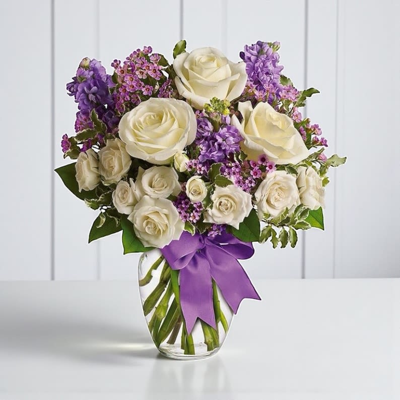 Enchanted Cottage Bouquet - This elegant bouquet carries a cozy countryside feel. Enchanted Cottage Bouquet is as enchanting as coming across a hidden cottage in the countryside! With its perfect purples and pearly whites, our unique cottage flower bouquet is great for display in any home or office. Lush white roses and purple stock mix with delicate lavender waxflower and green pitta negra for an elegant English garden look. The decorative bouquet is finished with a pretty satin ribbon.  White roses meet lavender stock and waxflower in this lush, elegant arrangement. Presented in a classic clear glass vase with purple satin ribbon. Orientation: One-Sided  Details:  Standard - 16 1/2&quot; H by 14 1/2&quot; W Deluxe - 17 1/2&quot; H by 15 1/2&quot; W Premium - 18 1/2&quot; H by 15 1/2&quot; W