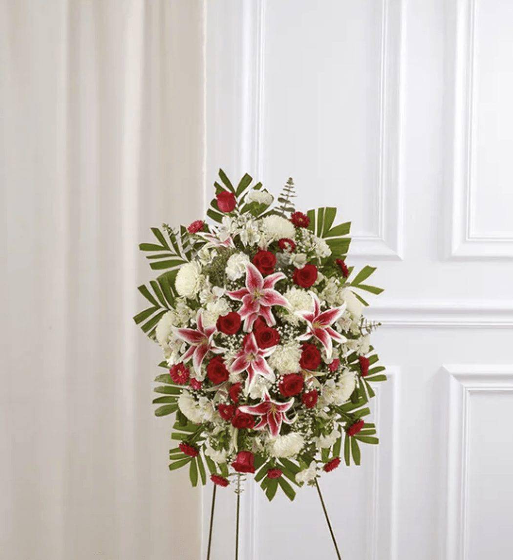 Red Rose And Lily Standing Spray - Celebrate a beautiful life with a truly heartfelt gesture. Our elegant standing sympathy spray is arranged with a gathering of radiant red, soft pink and pure white blooms. A traditional floral display for the services, it’s a touching way to honor the memory of a loved one while expressing your deepest condolences.  One-sided standing spray arrangement with red roses and Matsumoto asters, pink Stargazer lilies, white Peruvian lilies (alstroemeria), carnations and football mums; accented with spiral and seeded eucalyptus, baby’s breath and assorted greenery    